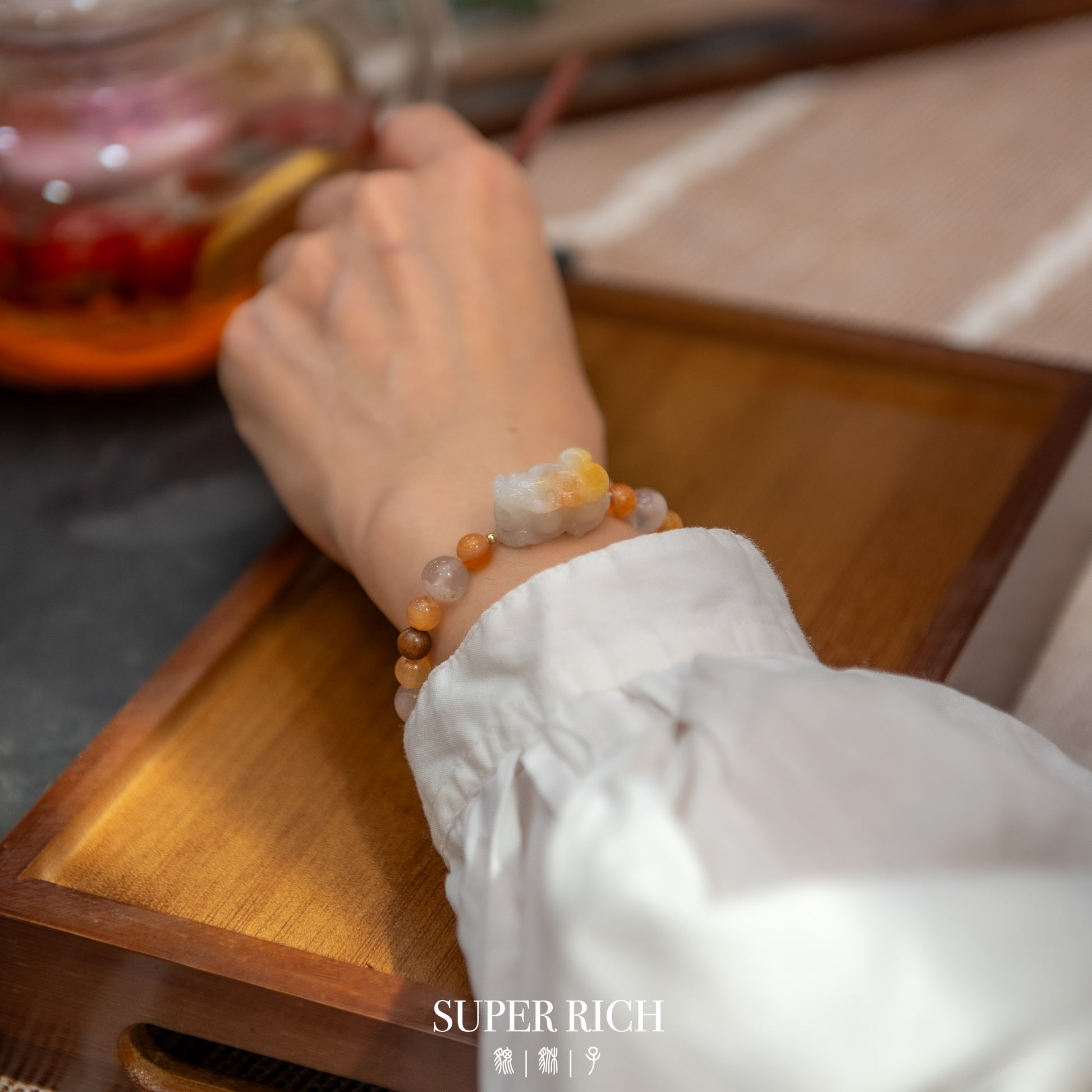 Hand wearing a bracelet on a wooden surface with 'SUPER RICH' branding.