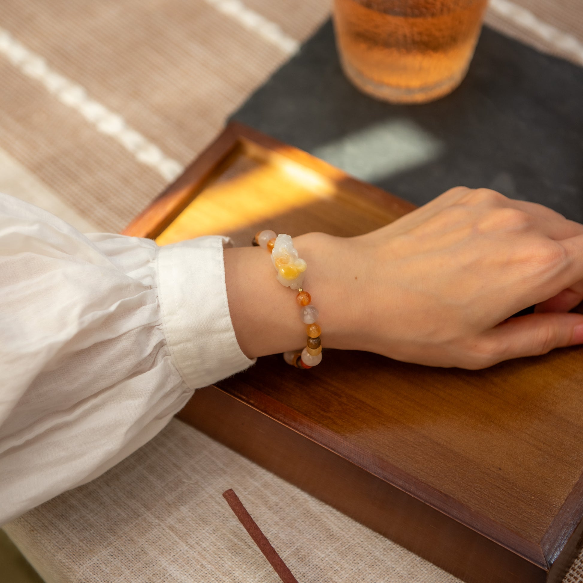 Person wearing a beaded bracelet on a wooden surface with a glass of beer in the background