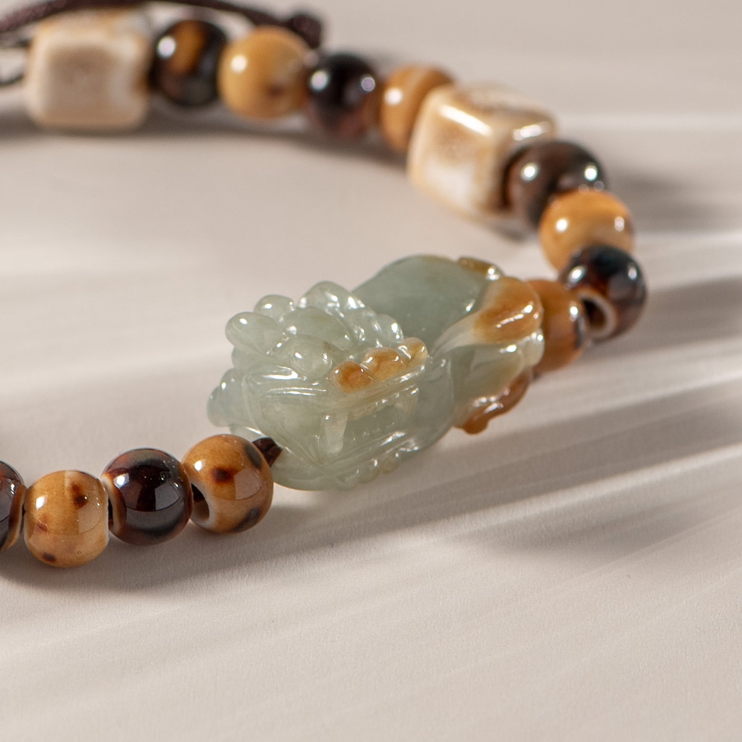 Bracelet with brown and black beaded chain and a green jade pendant on a beige background