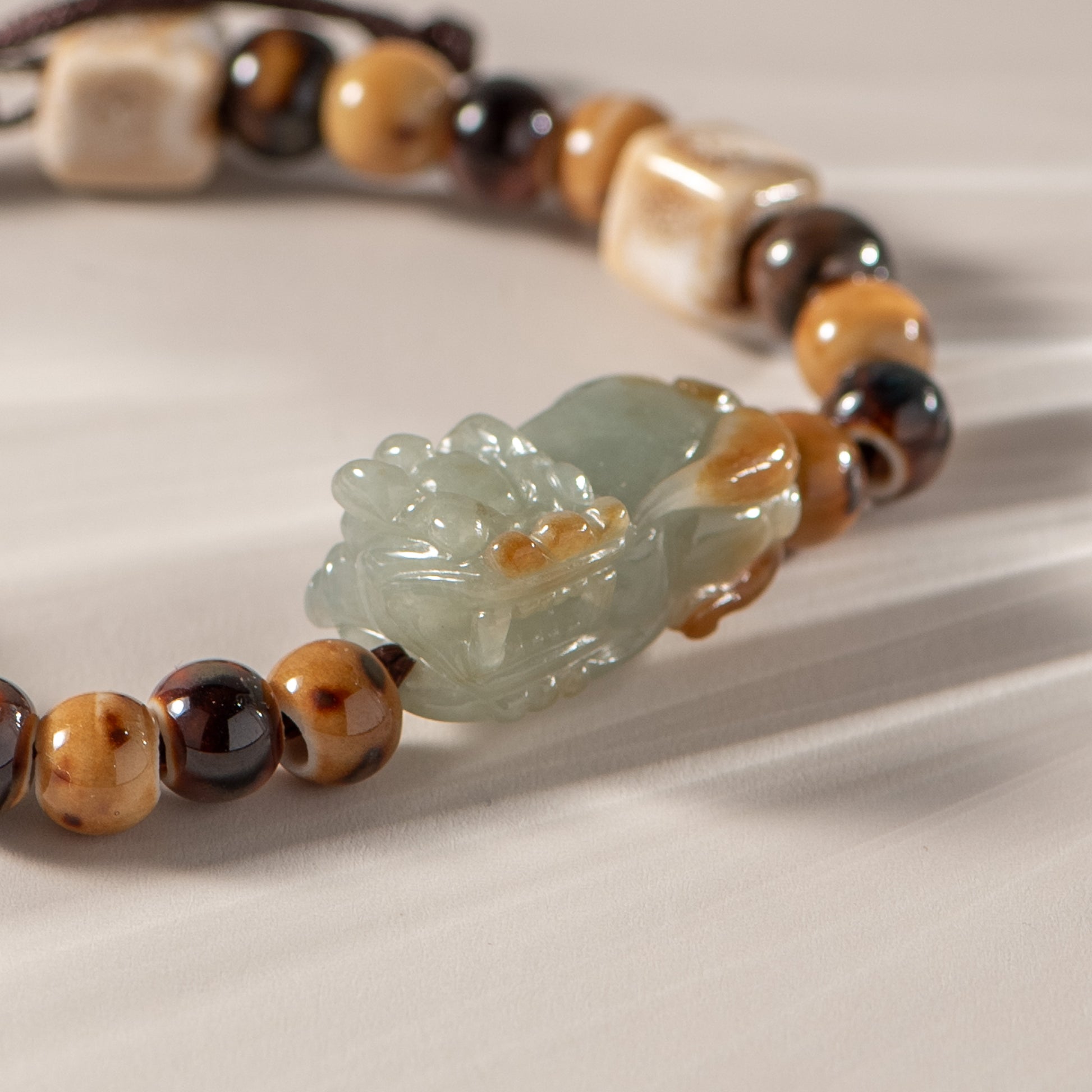 Bracelet with brown and black beaded chain and a green jade pendant on a beige background