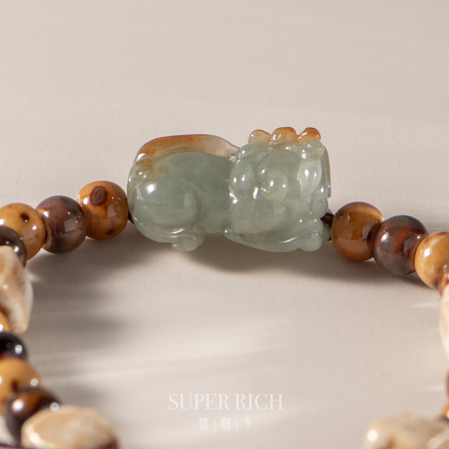 Close-up of a beaded bracelet with a jade cat figure on a neutral background