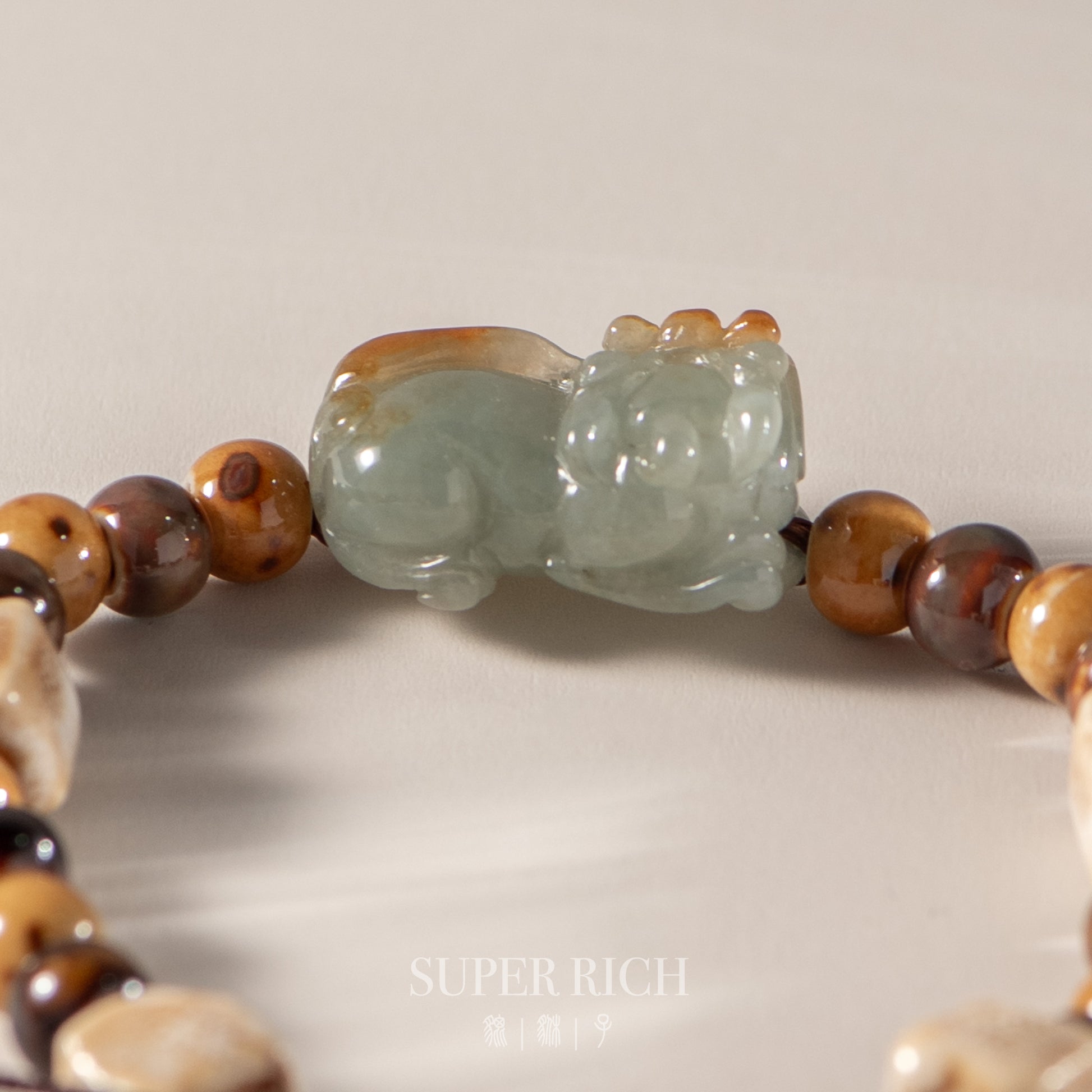 Close-up of a beaded bracelet with a jade cat figure on a neutral background