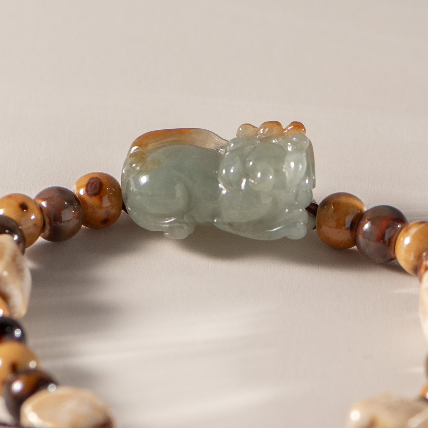 Close-up of a bracelet with a jade cat bead on a neutral background