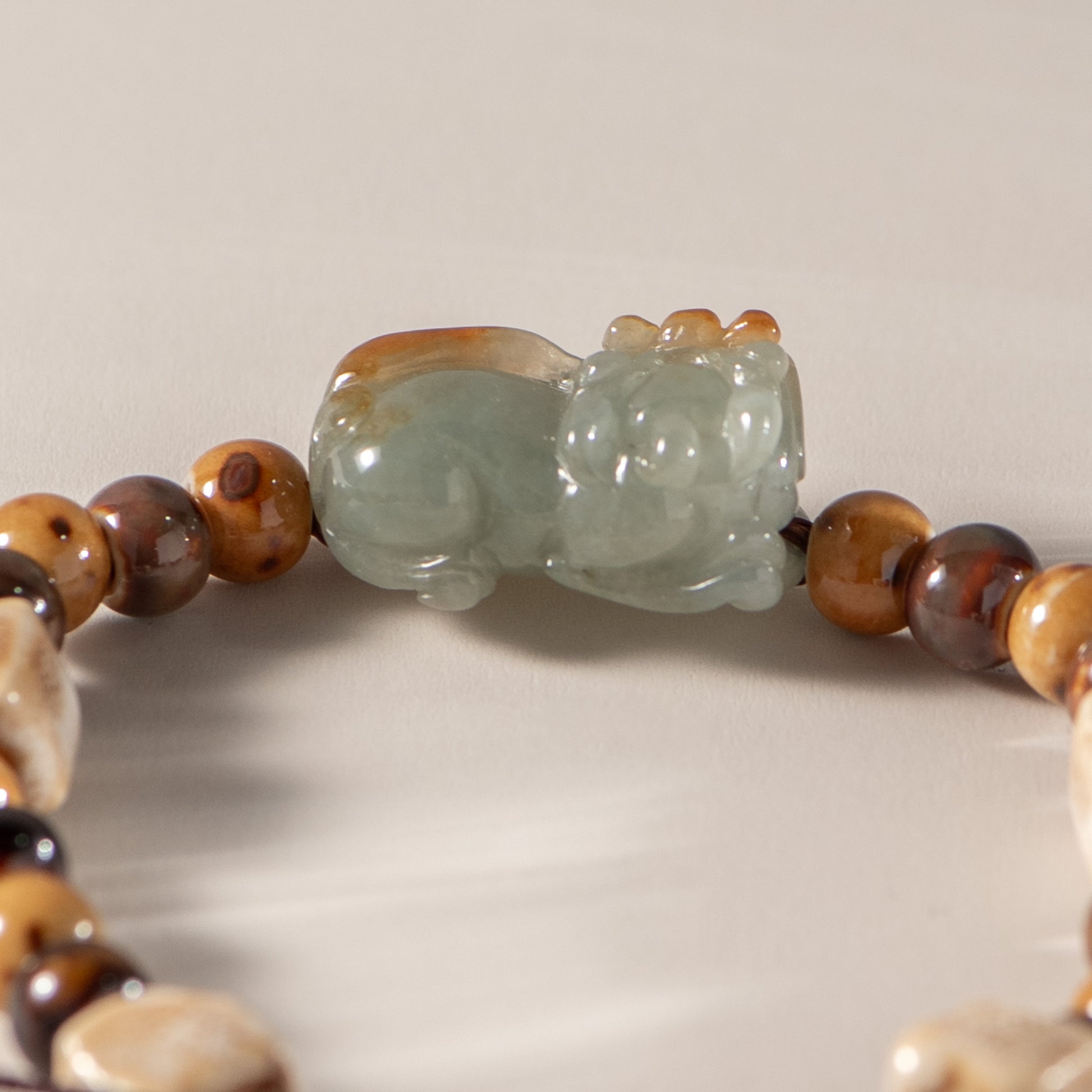 Close-up of a bracelet with a jade cat bead on a neutral background