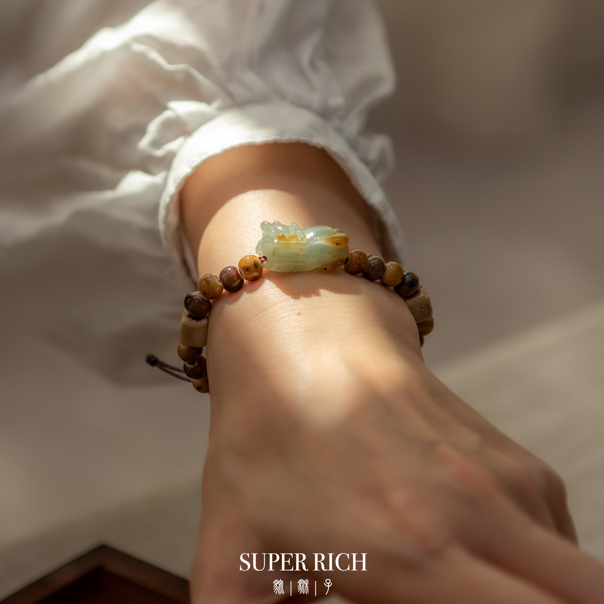 Close-up of a wrist wearing a bracelet with a jade charm, with 'SUPER RICH' branding.