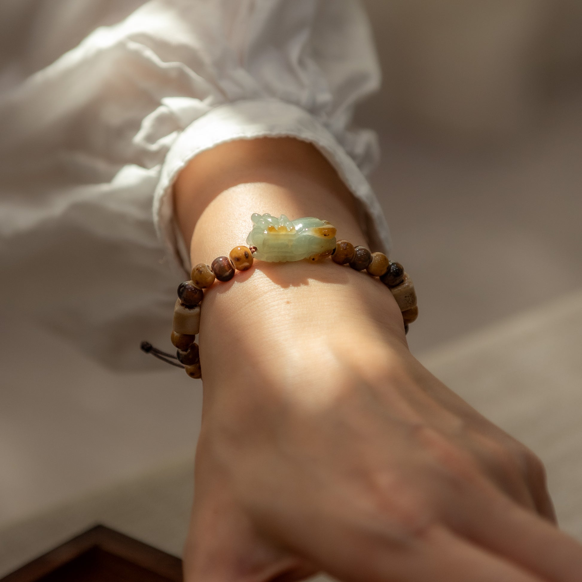 Hand wearing a bracelet with a jade charm on a neutral background