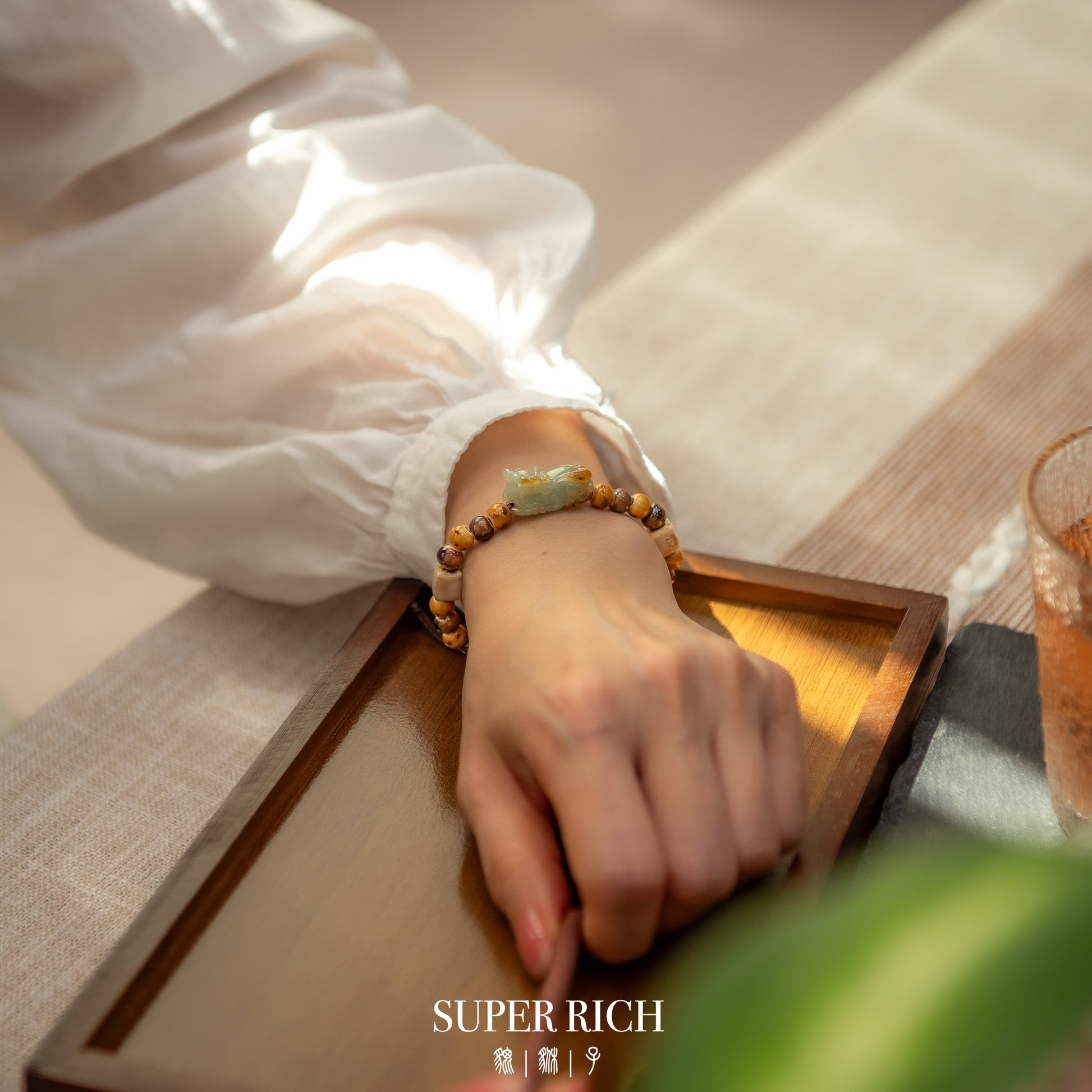 Hand wearing a beaded bracelet on a wooden surface with 'SUPER RICH' branding.