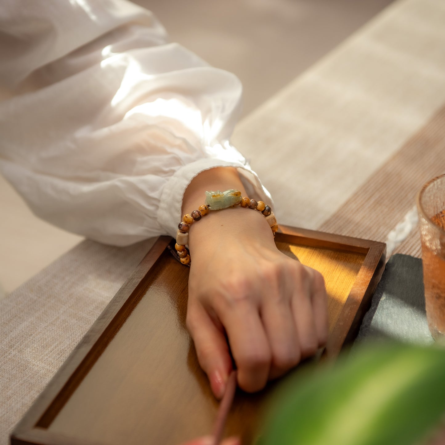 Hand wearing a beaded bracelet on a wooden surface with a blurred background