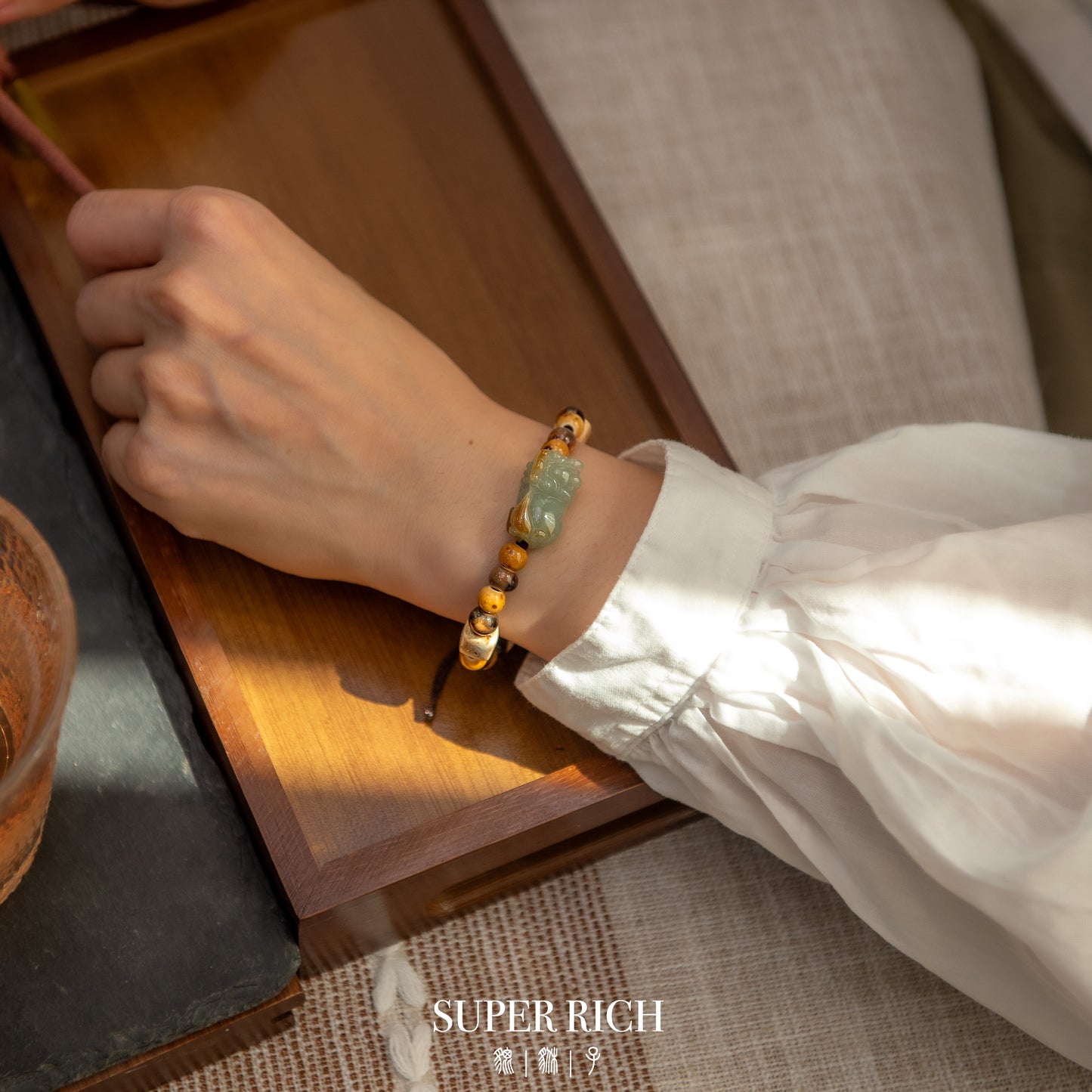 Hand wearing a bracelet with a wooden surface and tea cup in the background