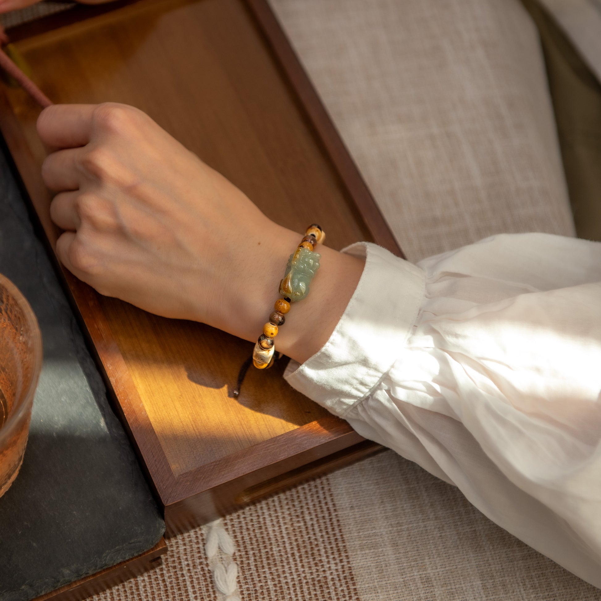 Hand wearing a beaded bracelet on a wooden surface with a cup of tea.