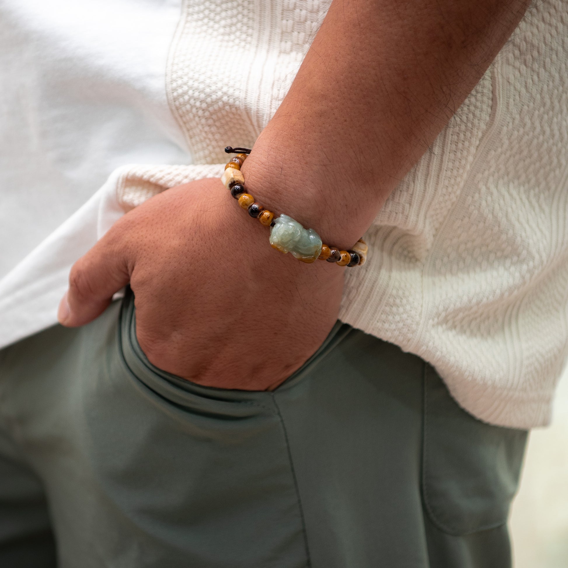 Person wearing a bracelet with a green stone and brown beads, holding a white shirt.