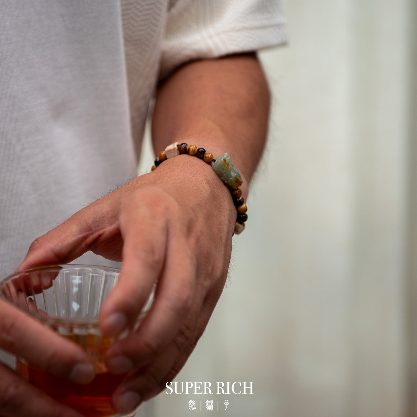 Person holding a glass with a blurred background and 'SUPER RICH' branding.