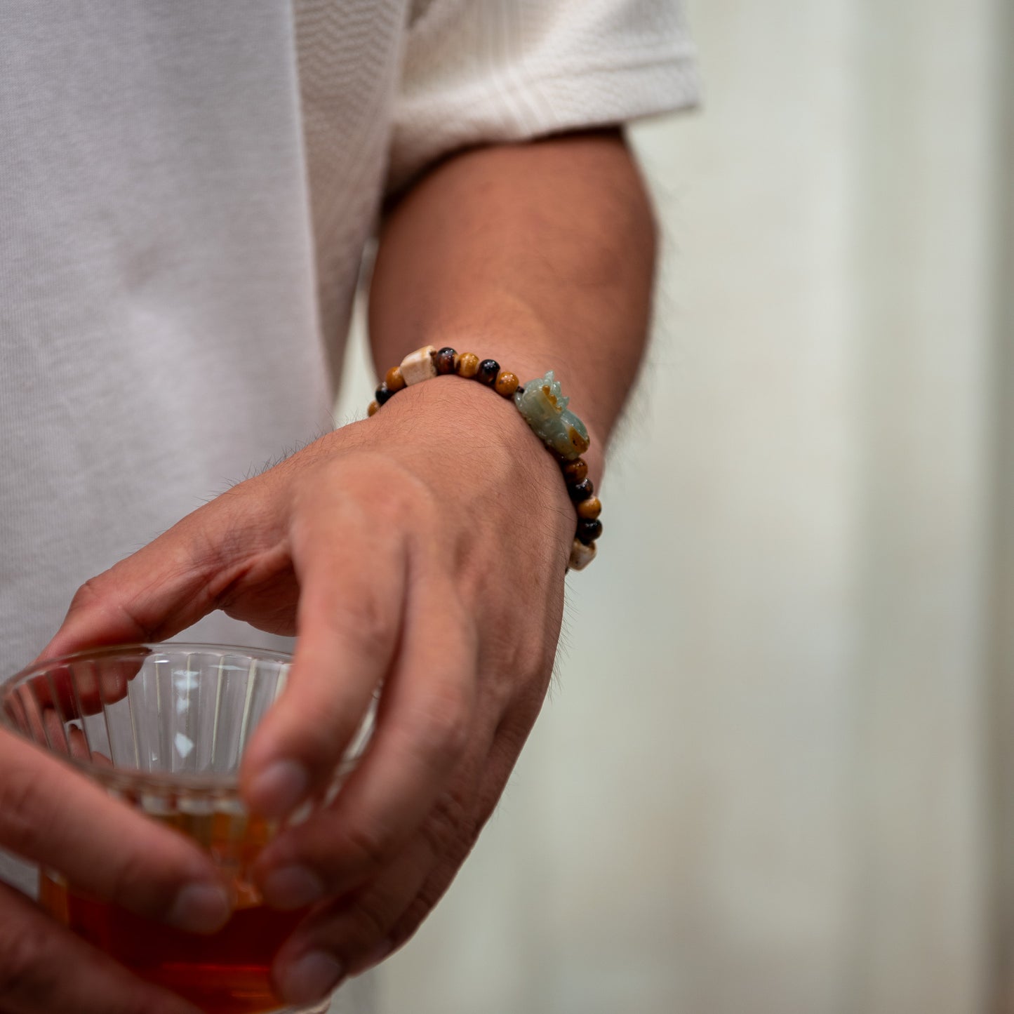 Person holding a glass with a drink, wearing a bracelet on a blurred background