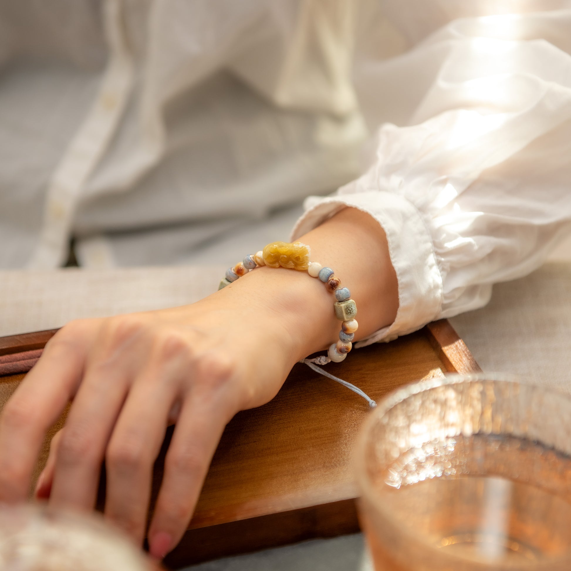 Person wearing a bracelet with small beads on a wooden table.