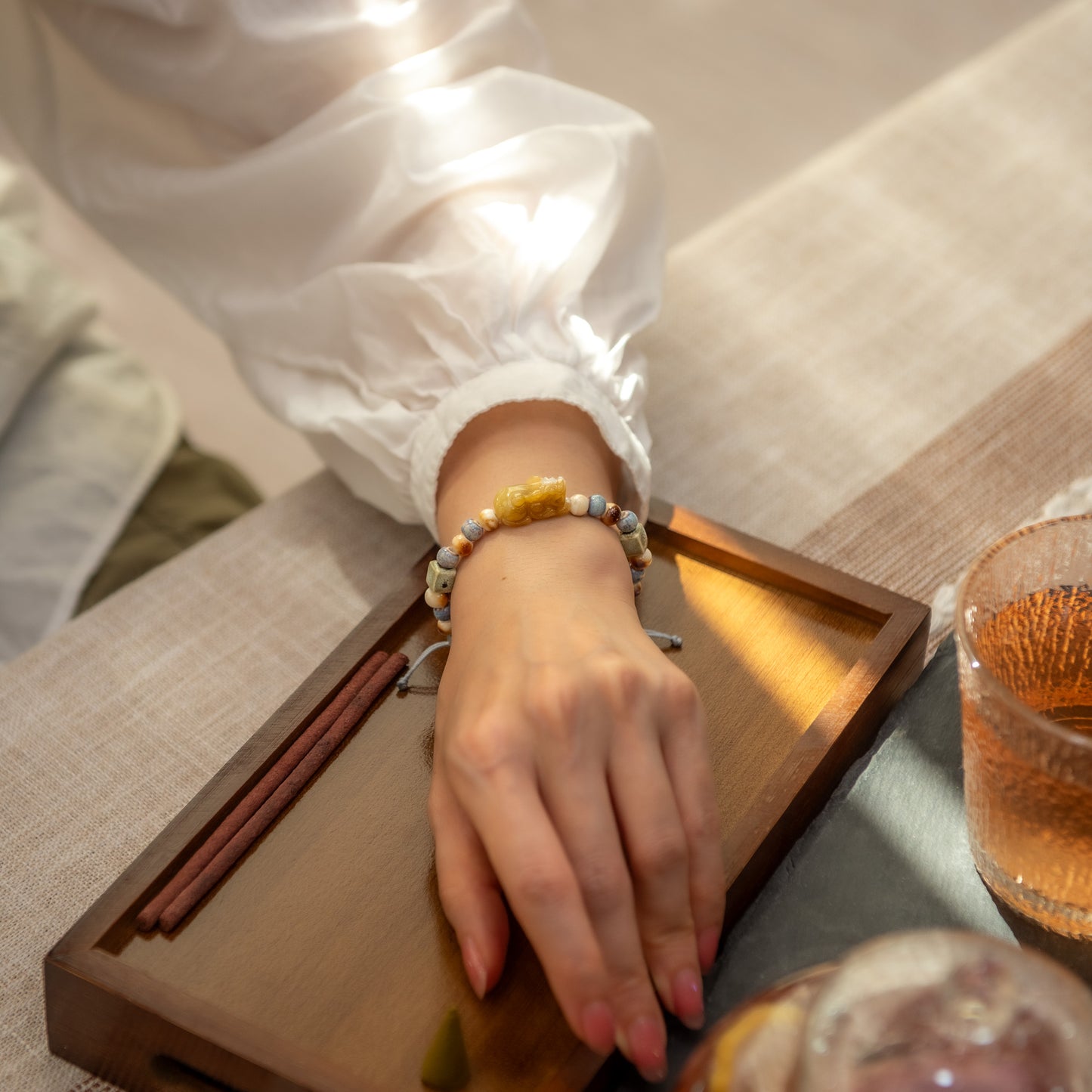 Person's hand wearing a bracelet on a wooden tray with a glass of tea.
