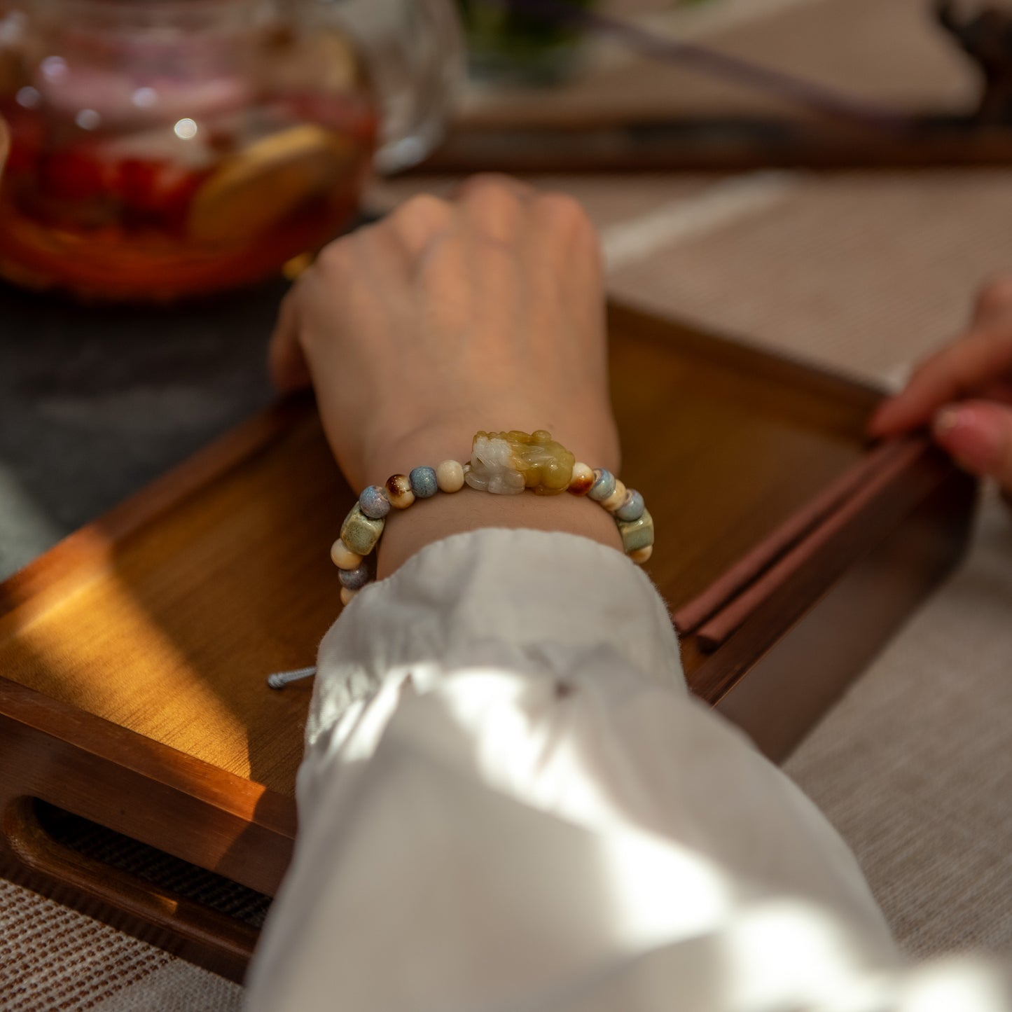 Person wearing a colorful beaded bracelet on a wooden table with a blurred background