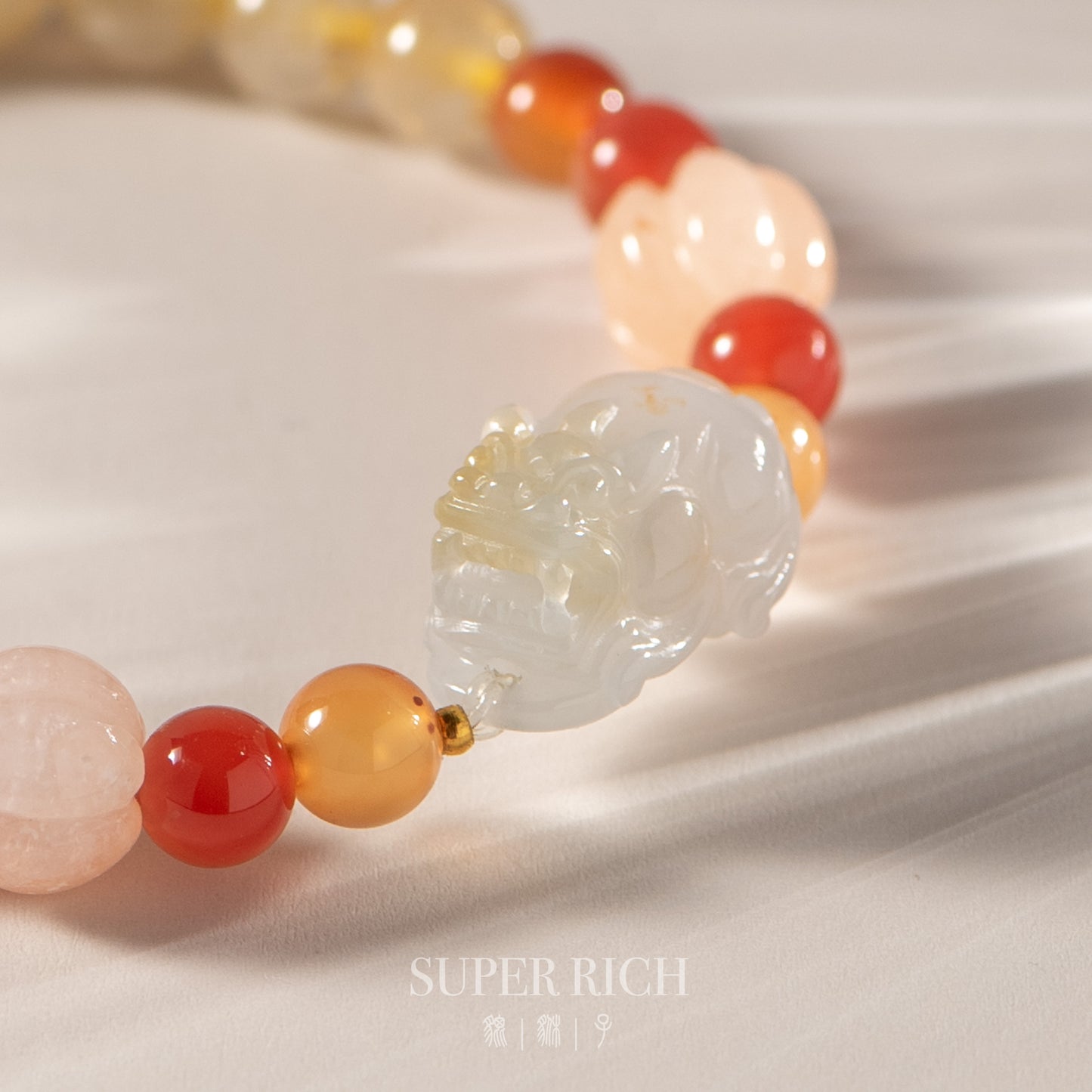 Bracelet with multicolored beads and a jade pendant on a white fabric background, featuring the brand 'SUPER RICH'.