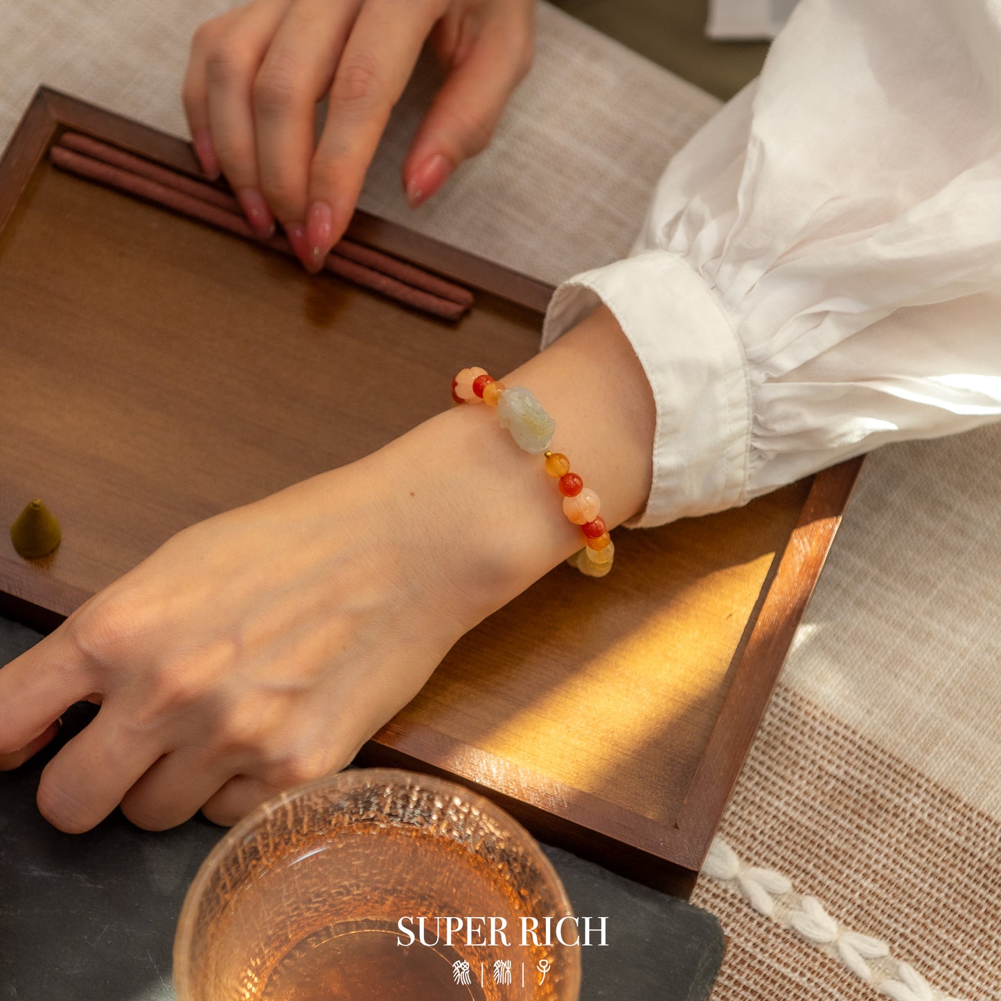 Person wearing a colorful beaded bracelet on a wooden surface with 'SUPER RICH' branding.