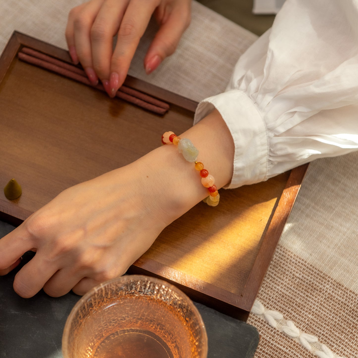 Person wearing a colorful beaded bracelet at a tea ceremony setup