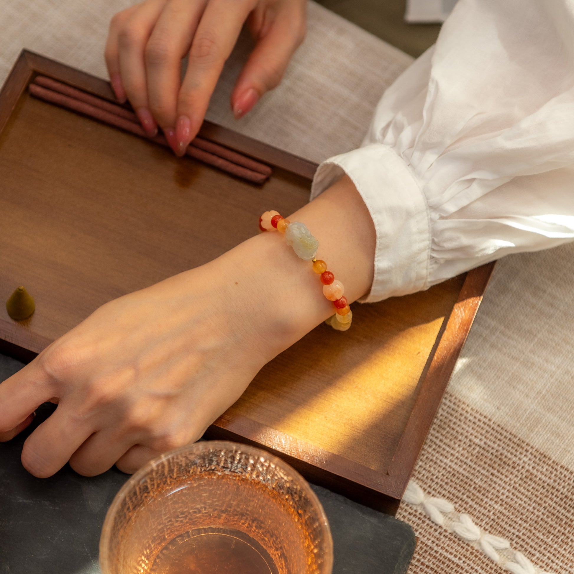 Person wearing a colorful beaded bracelet at a tea ceremony setup