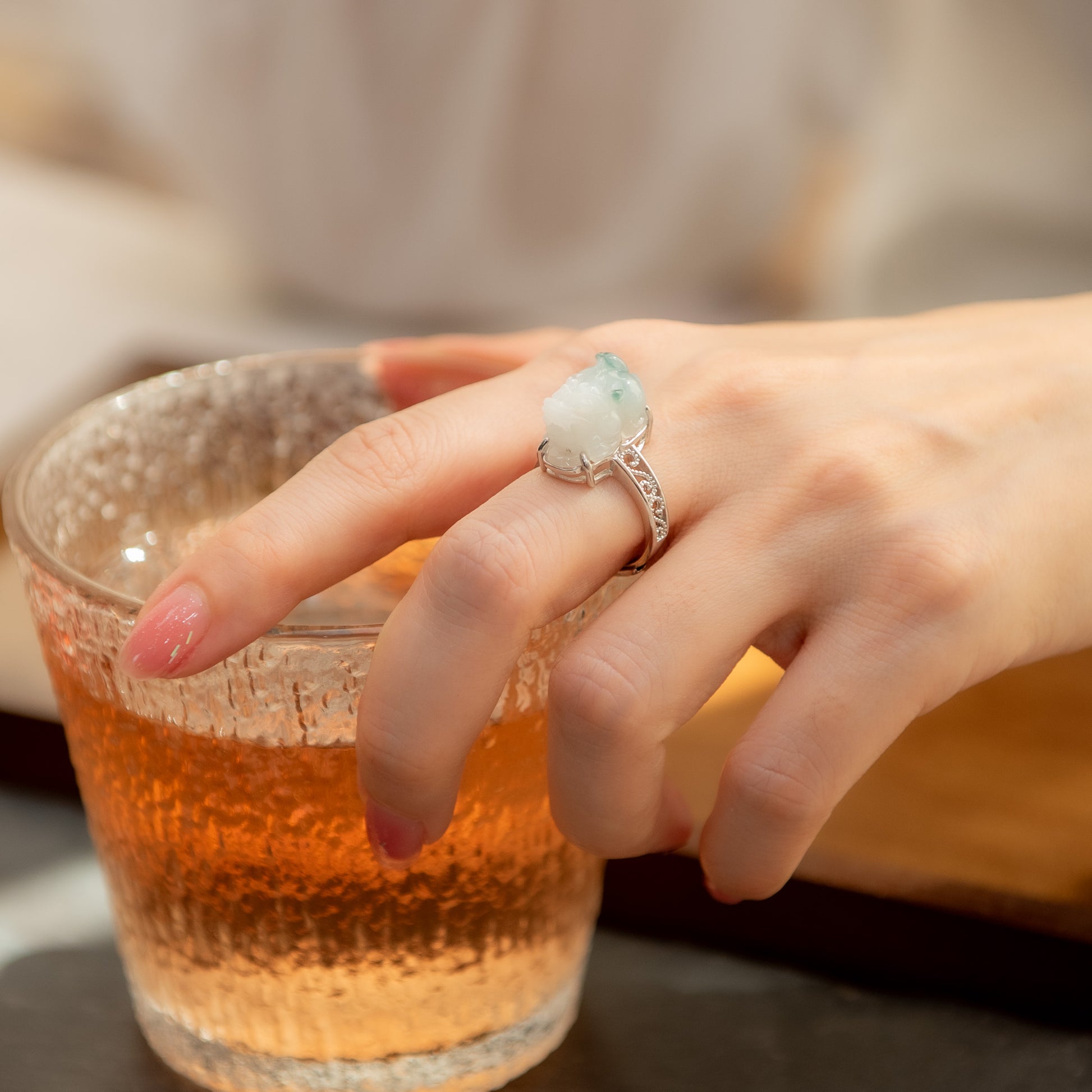 Hand with a decorative ring holding a glass of amber liquid.