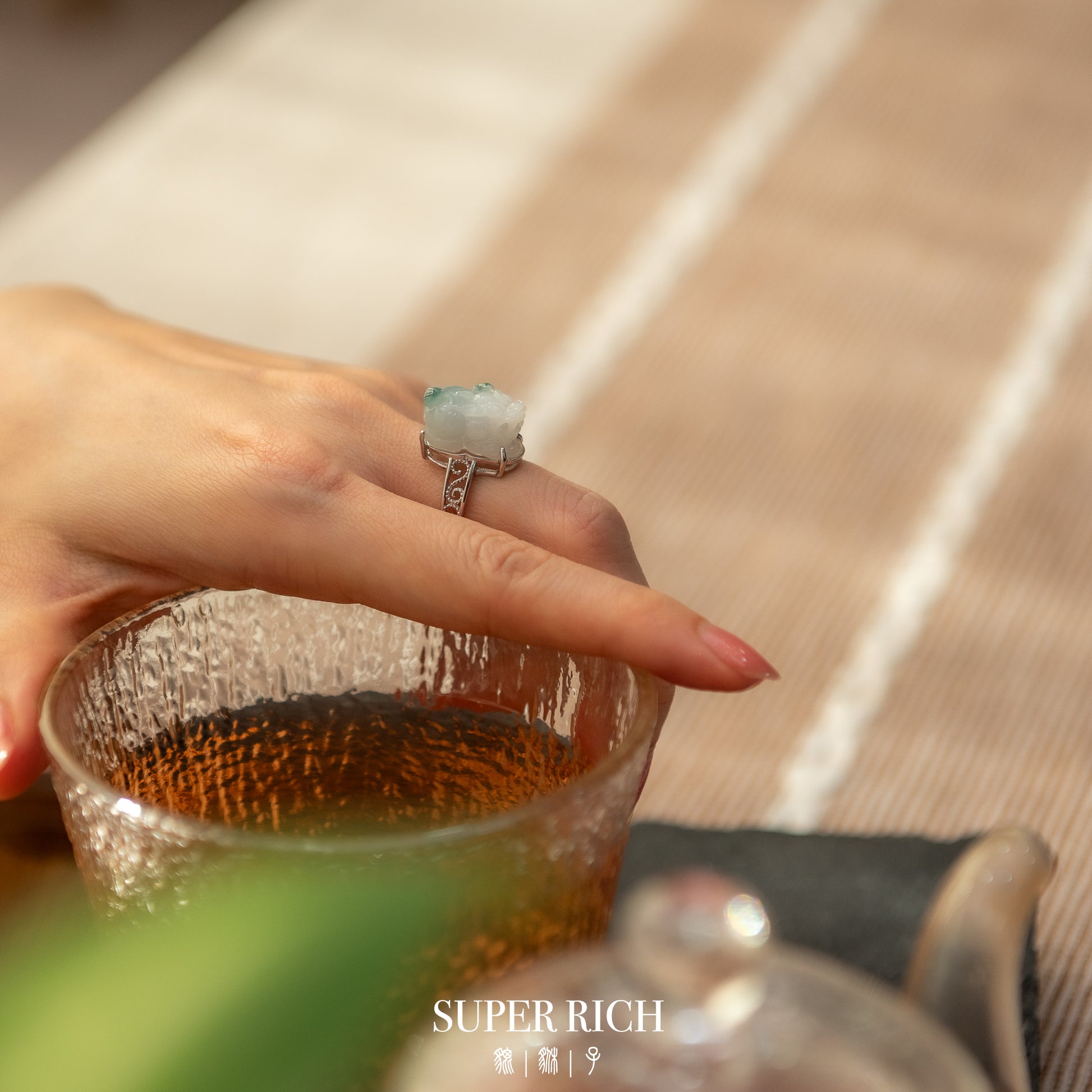 Hand holding a glass with a teacup and 'SUPER RICH' branding in the background