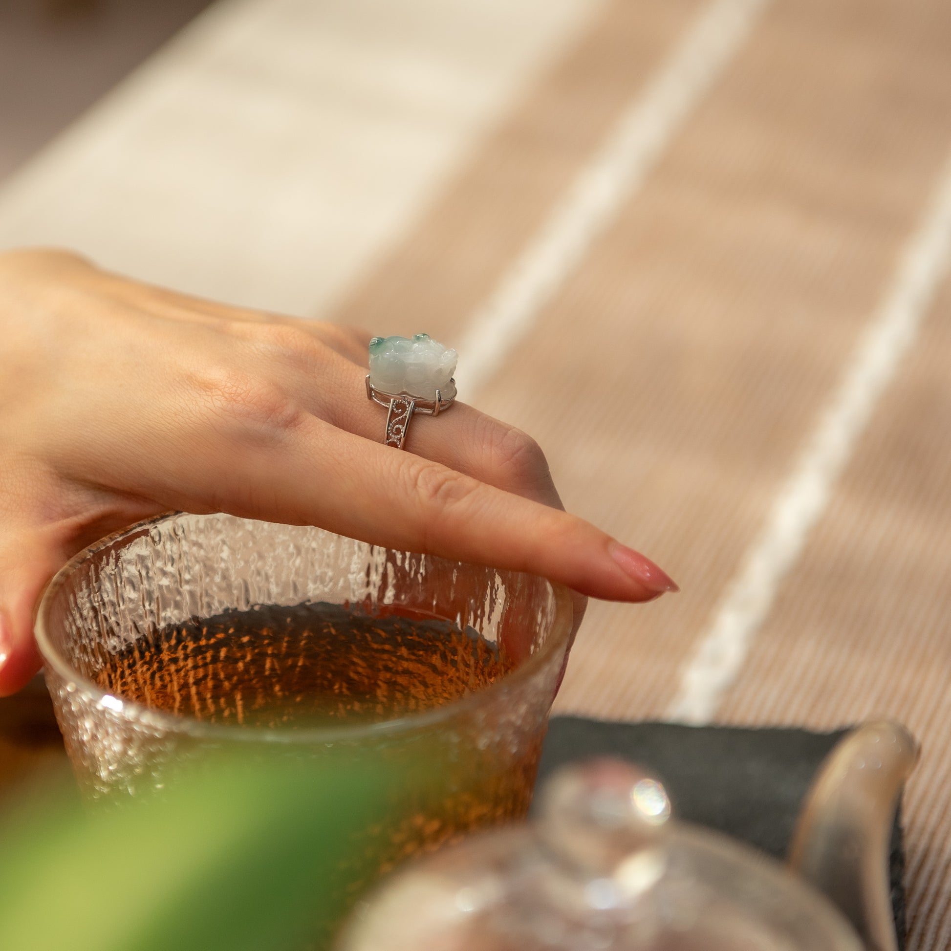 Hand holding a glass with a teacup and saucer in the background