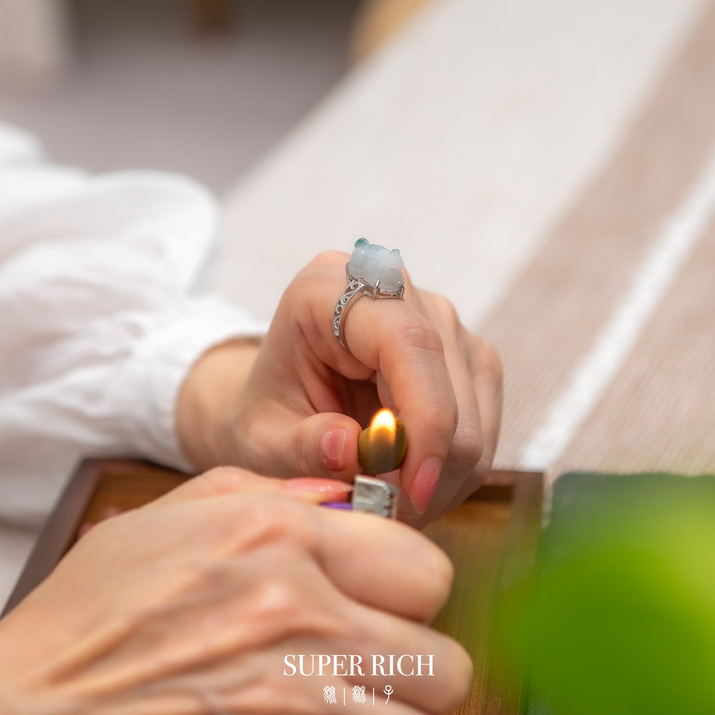 Close-up of hands lighting a candle with a 'Super Rich' product in the background