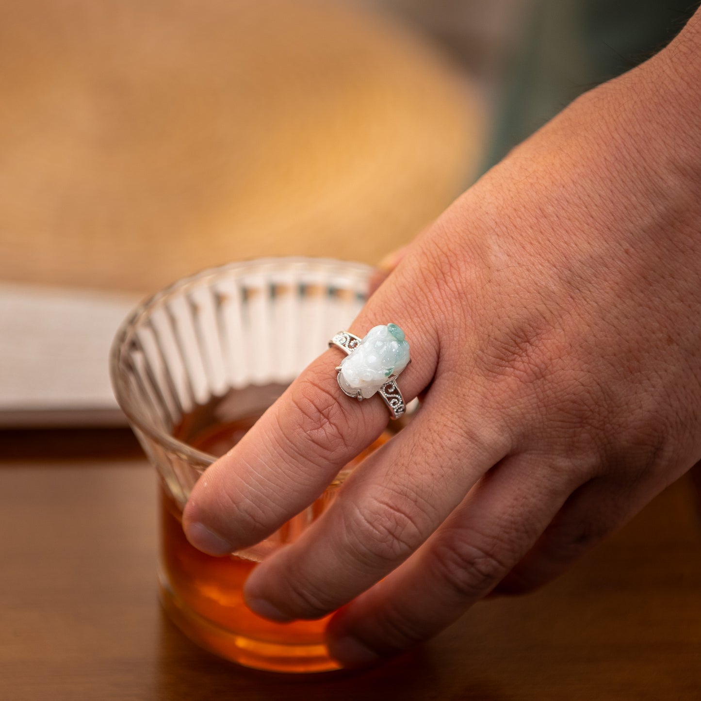 Hand holding a small glass of amber liquid with a decorative ring on a wooden surface
