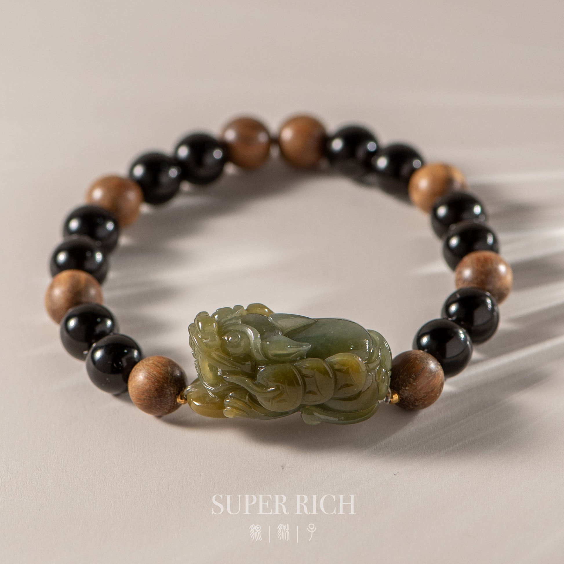 Bracelet with black, brown, and green beads featuring a carved stone charm on a beige background.