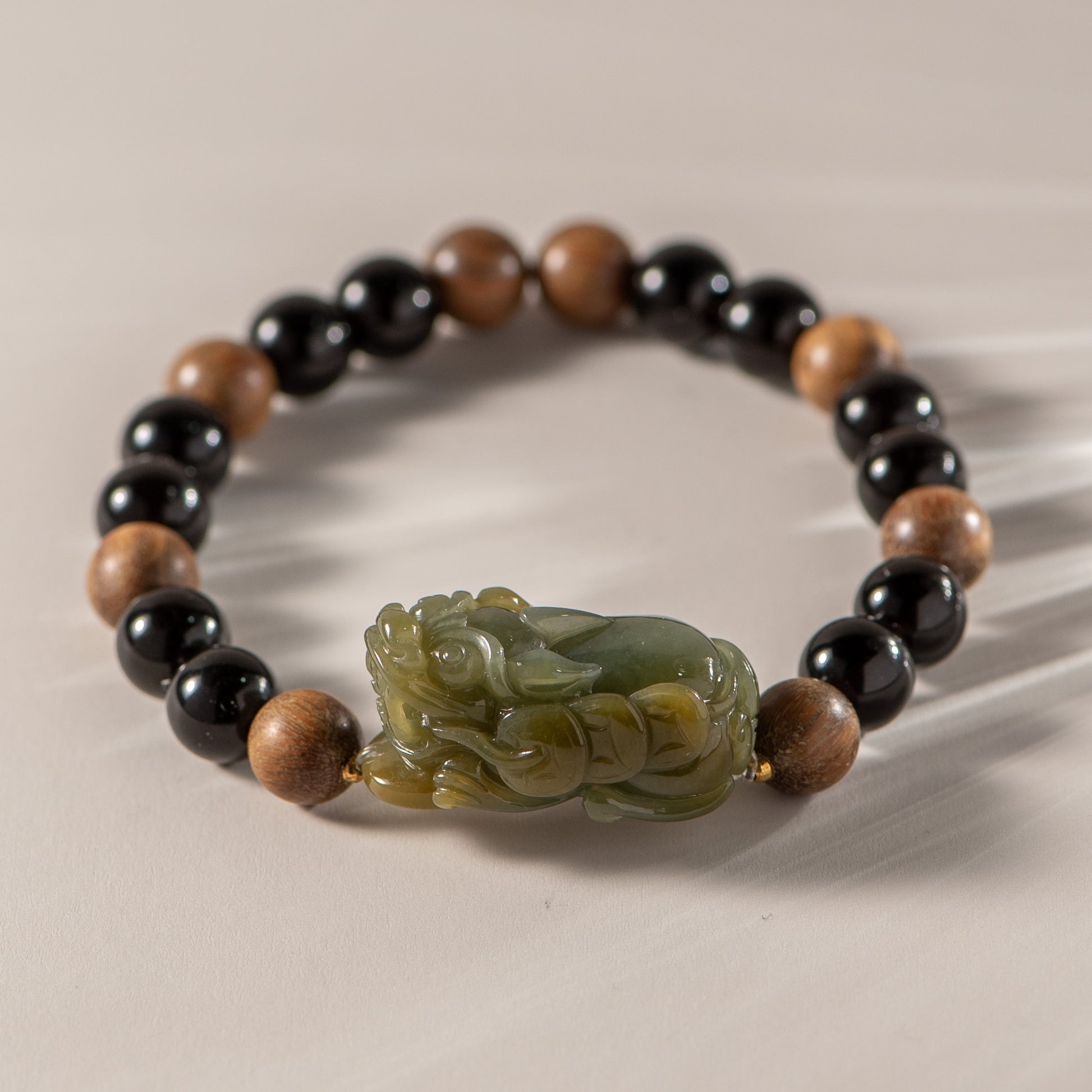 Bracelet with black, brown, and green beads featuring a carved stone charm on a beige background