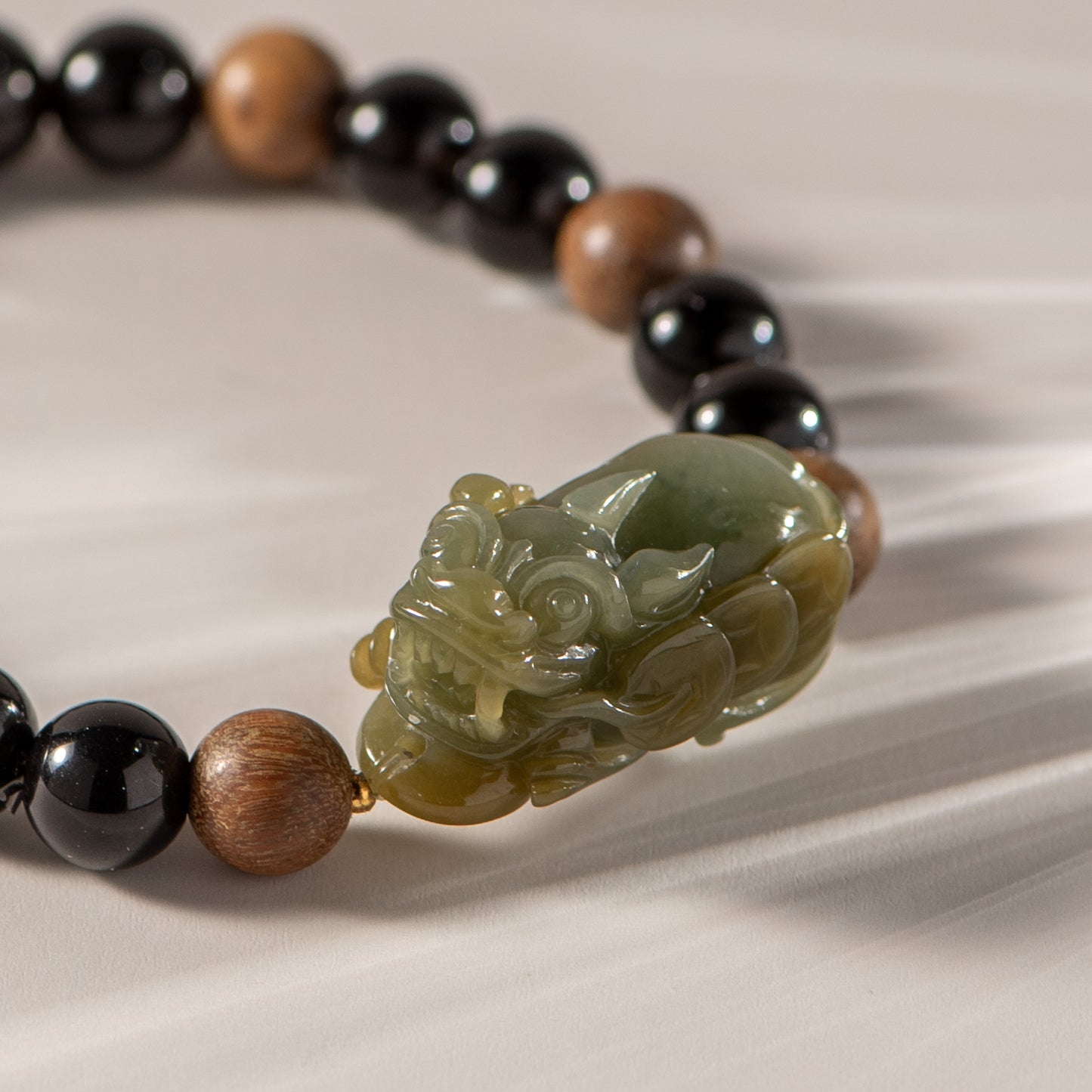 Bracelet with black, brown, and green beads featuring a carved stone bracelet on a beige fabric background.