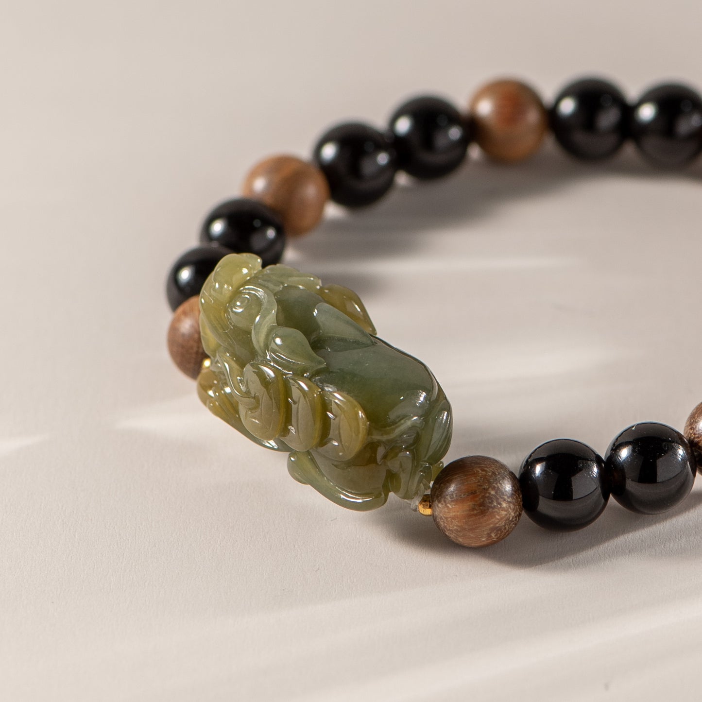 Bracelet with black, brown, and green beads featuring a carved stone charm on a beige background
