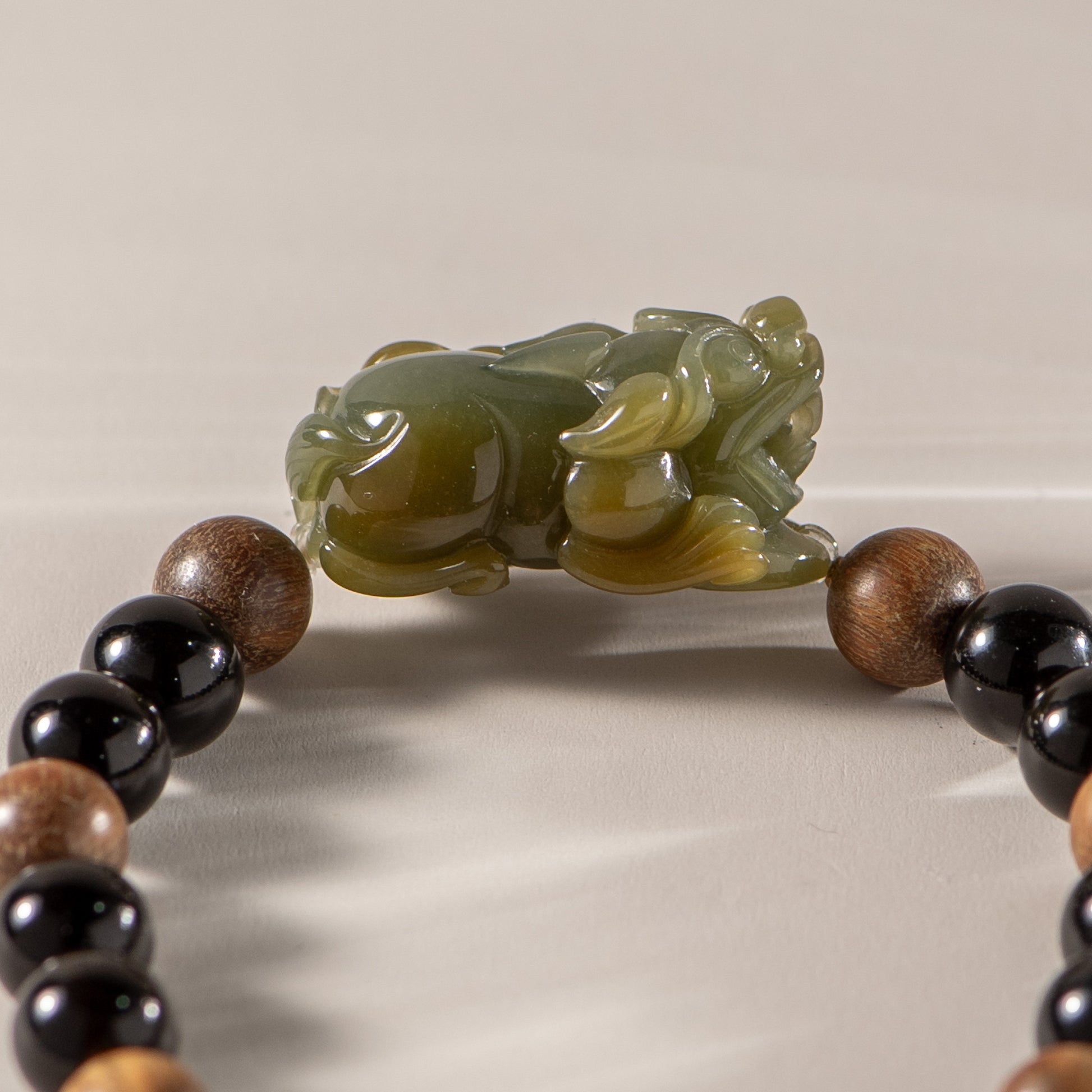 Bracelet with wooden and black beads featuring a green jade frog charm on a neutral background