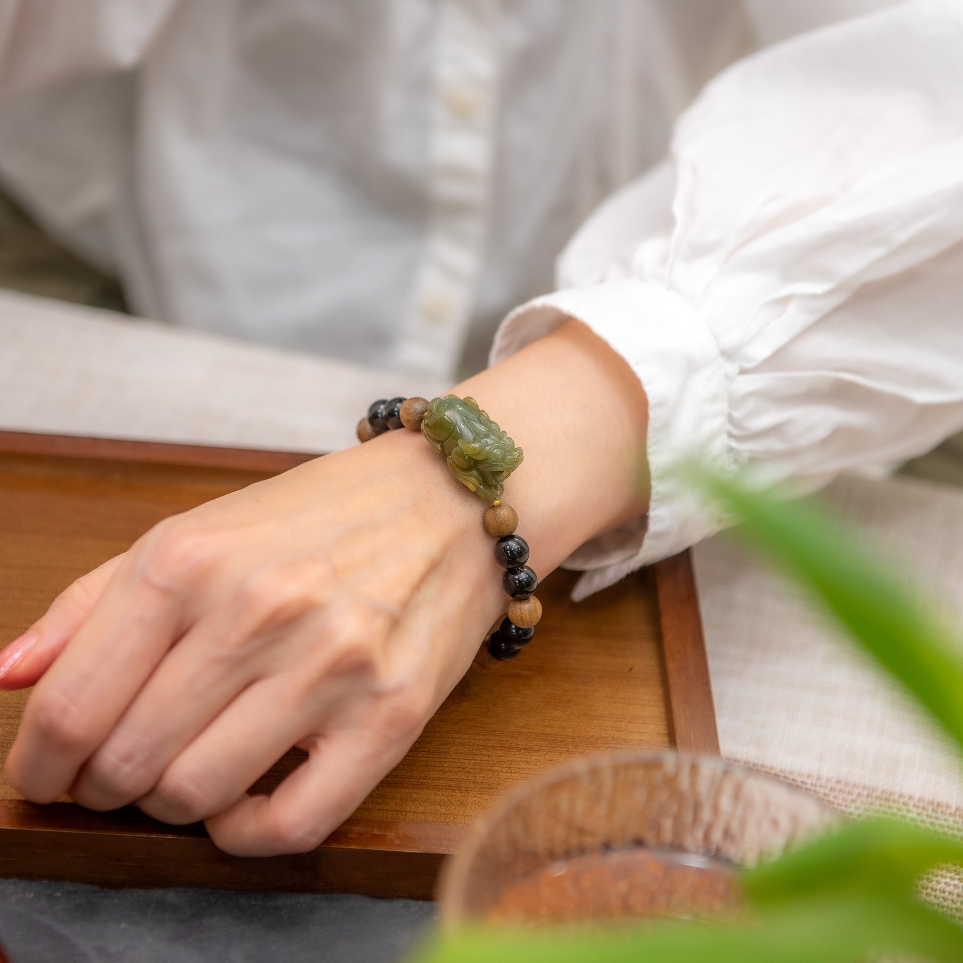 Person wearing a beaded bracelet on a wooden surface with a blurred background