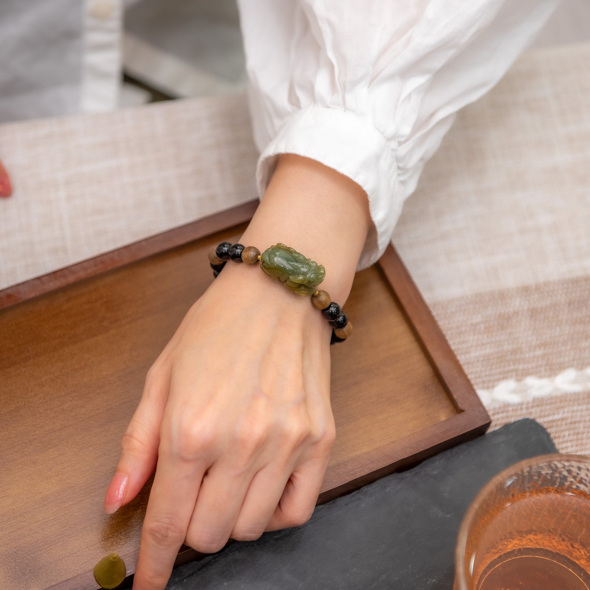 Hand wearing a bracelet with green beads on a wooden tray