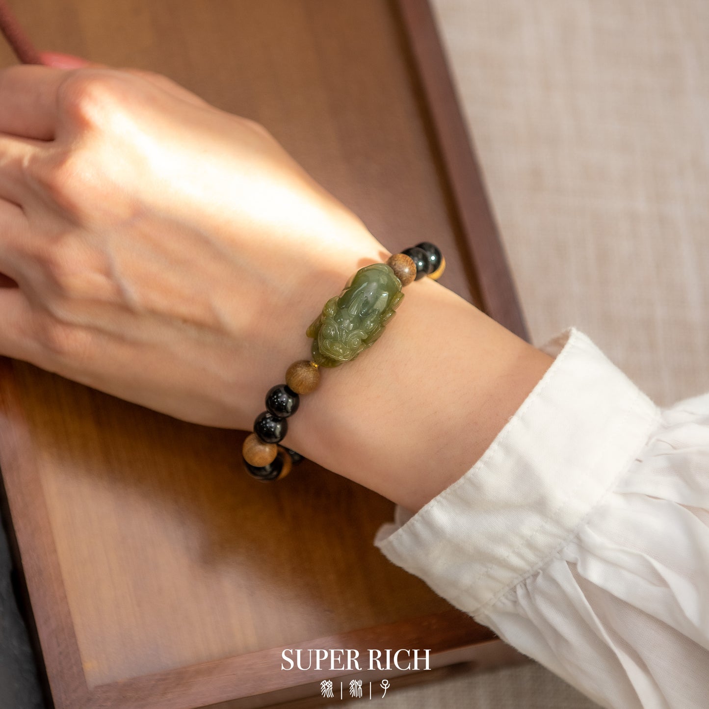 Hand wearing a green and black beaded bracelet on a wooden surface with 'SUPER RICH' branding.