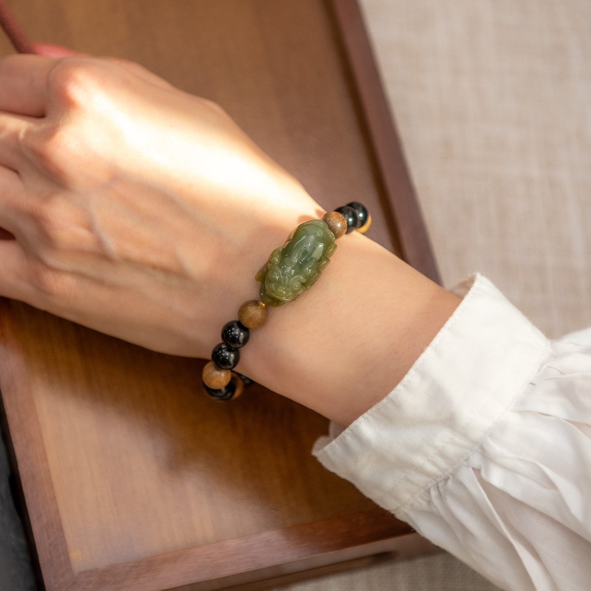 Person wearing a bracelet with green stone and black beads on a wooden surface