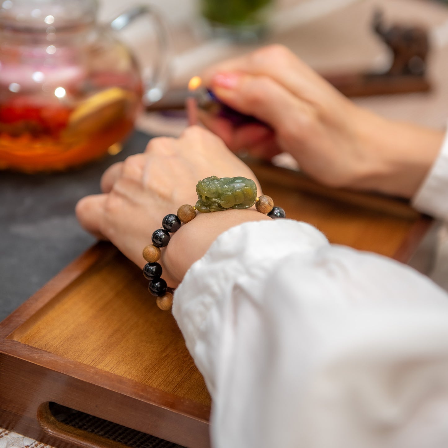 Person wearing a bracelet with a green stone on a wooden tray with a blurred background