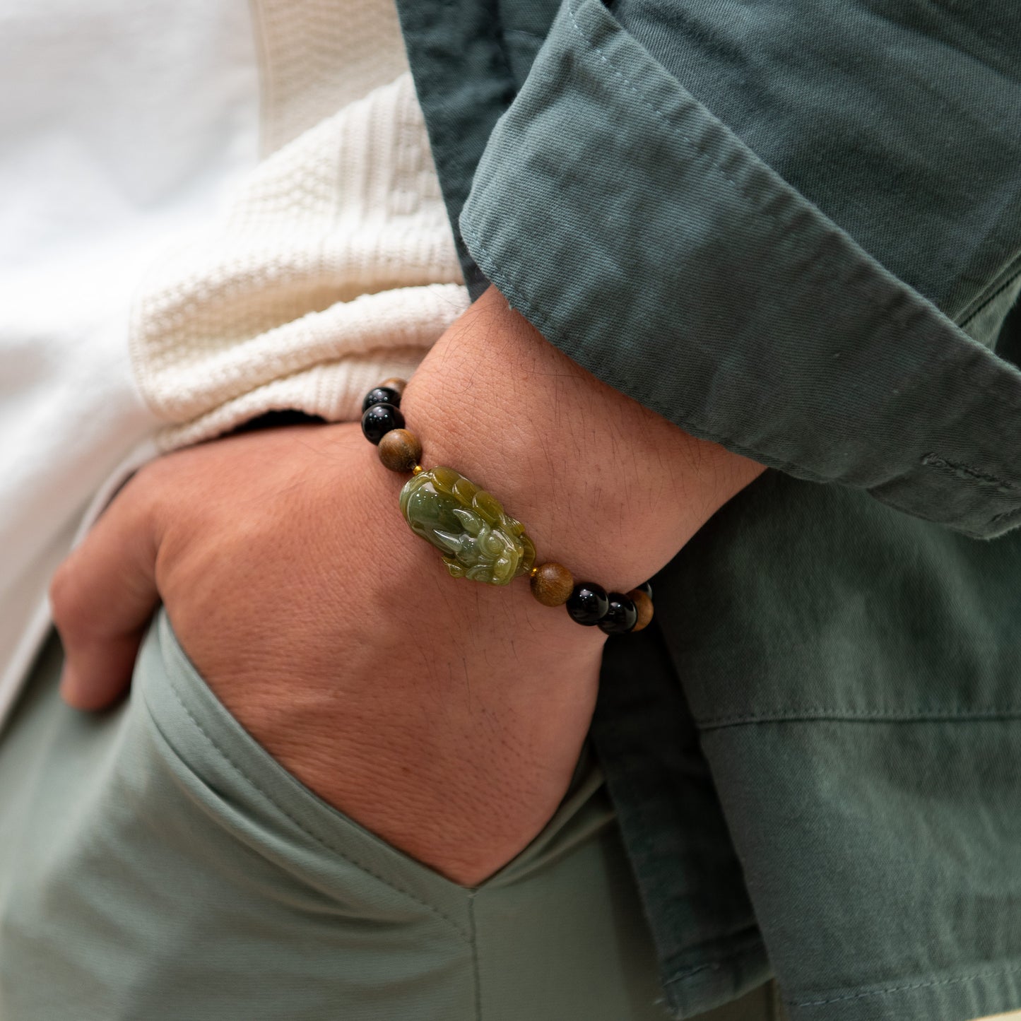 Close-up of a wrist wearing a bracelet with green and brown beads, against a neutral background.