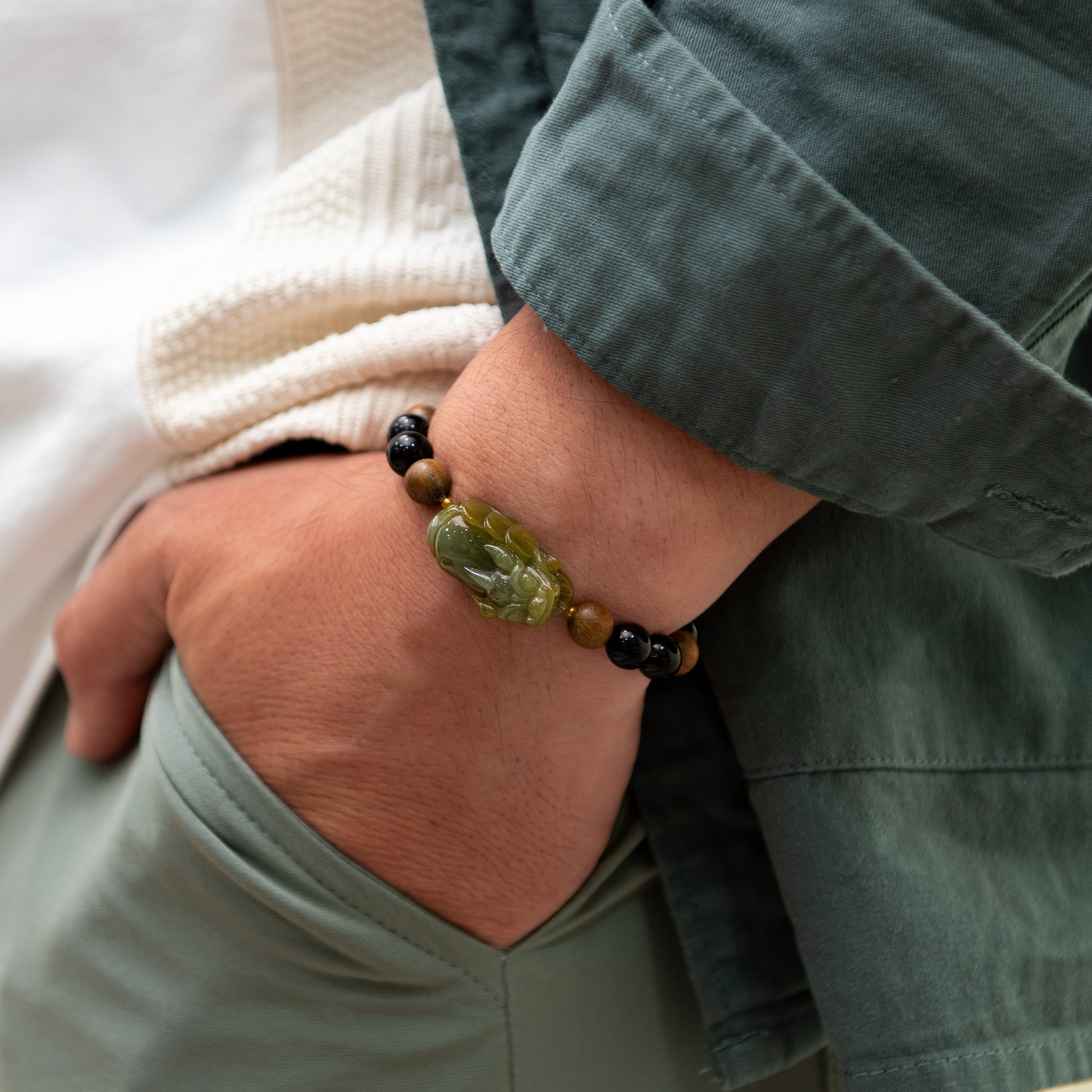 Close-up of a wrist wearing a bracelet with green and brown beads, against a neutral background.
