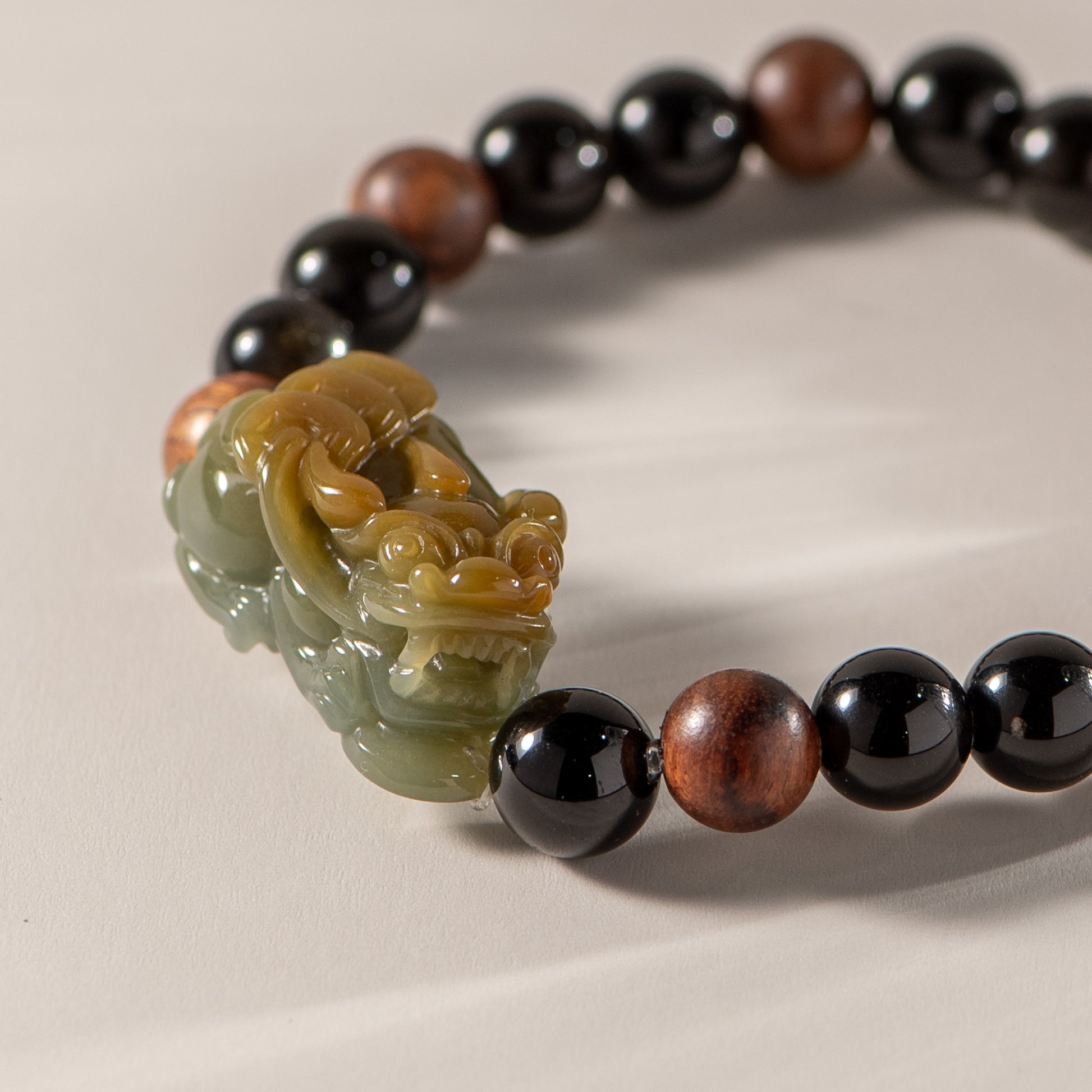 Beaded bracelet with a large green stone bead featuring a carved design on a beige background