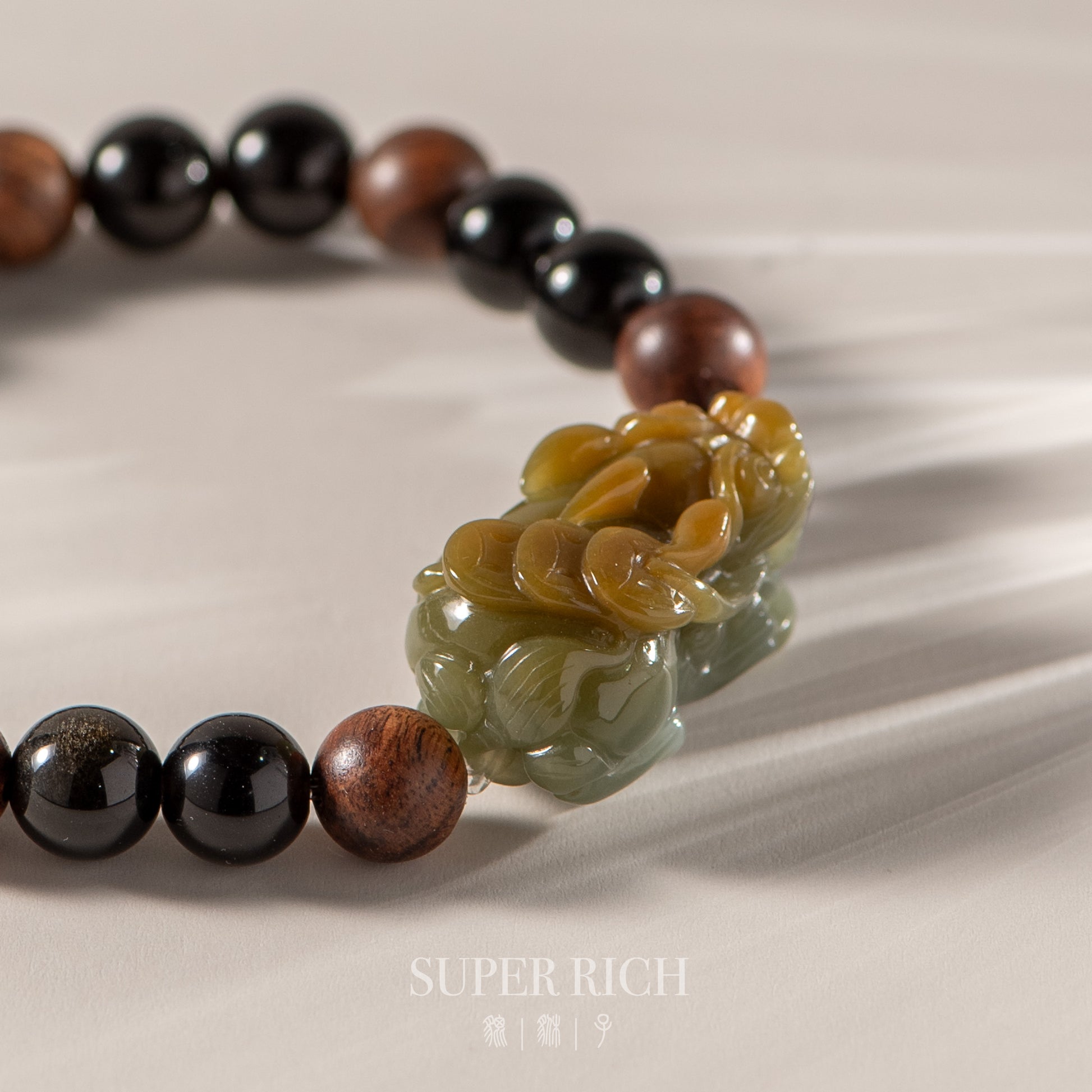 Jewelry with beads and a decorative green stone on a beige background, featuring the brand 'Super Rich'.