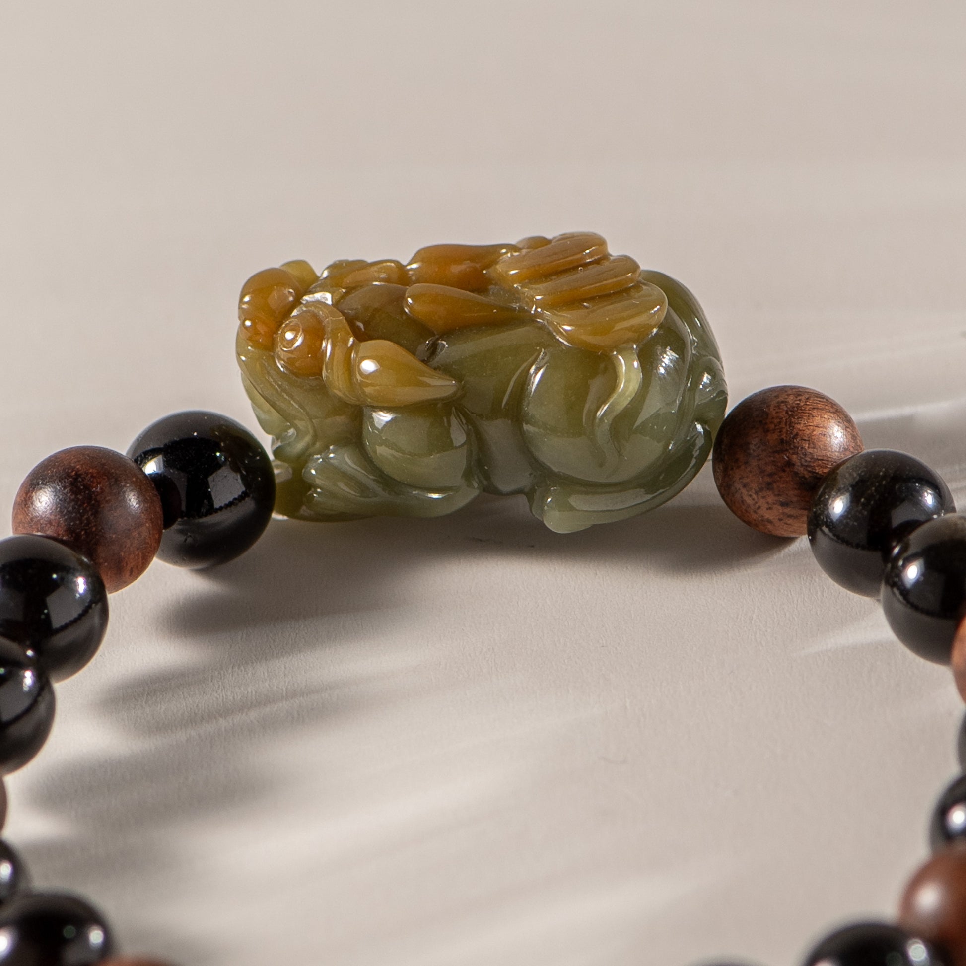 Close-up of a bracelet with a green jade charm and black beads on a neutral background
