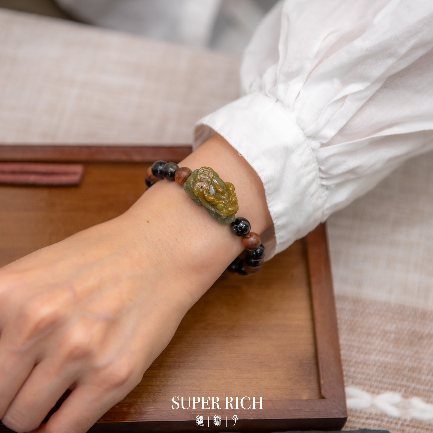 Close-up of a wrist wearing a decorative bracelet on a wooden surface with 'SUPER RICH' branding.