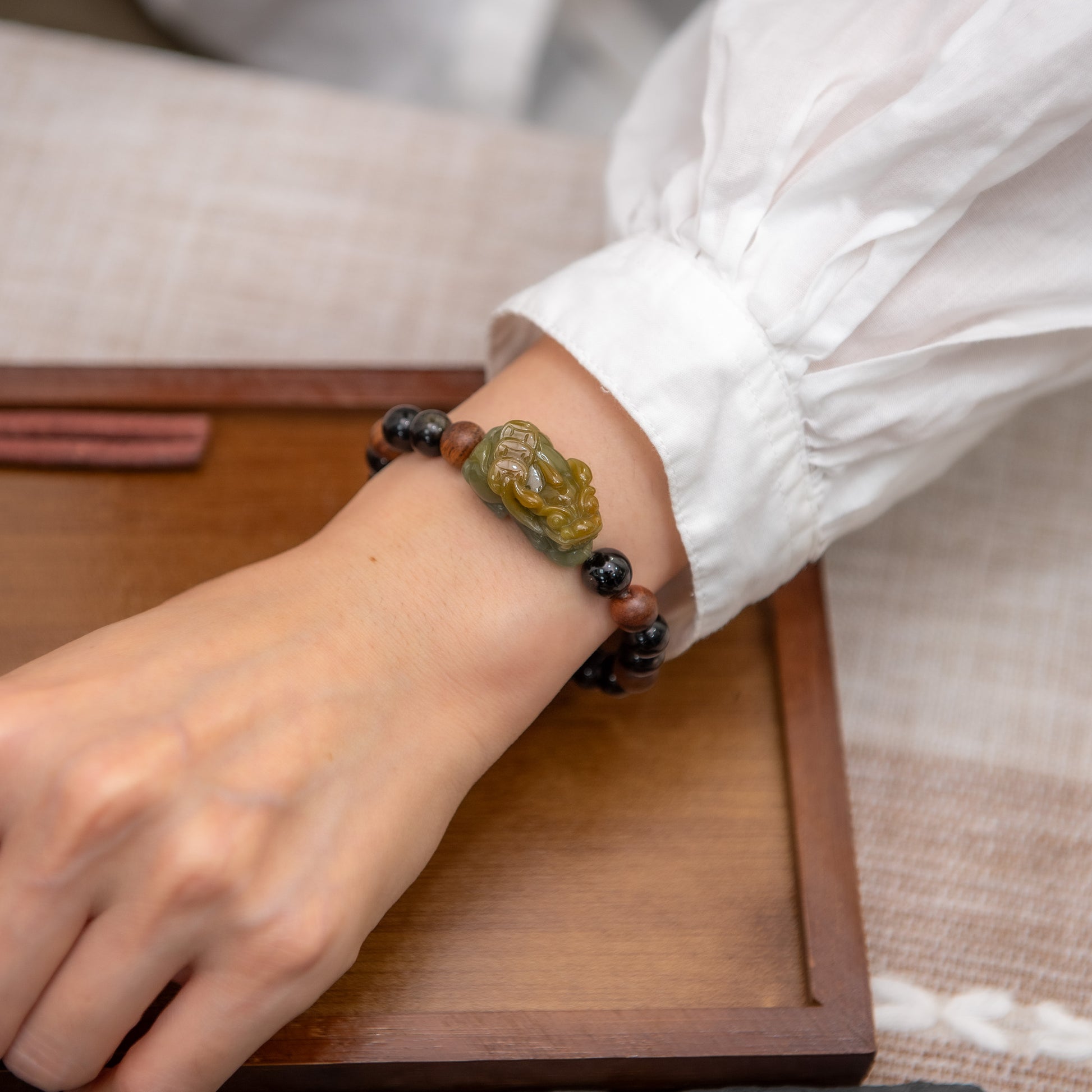 Person wearing a bracelet with a decorative charm on a wooden surface