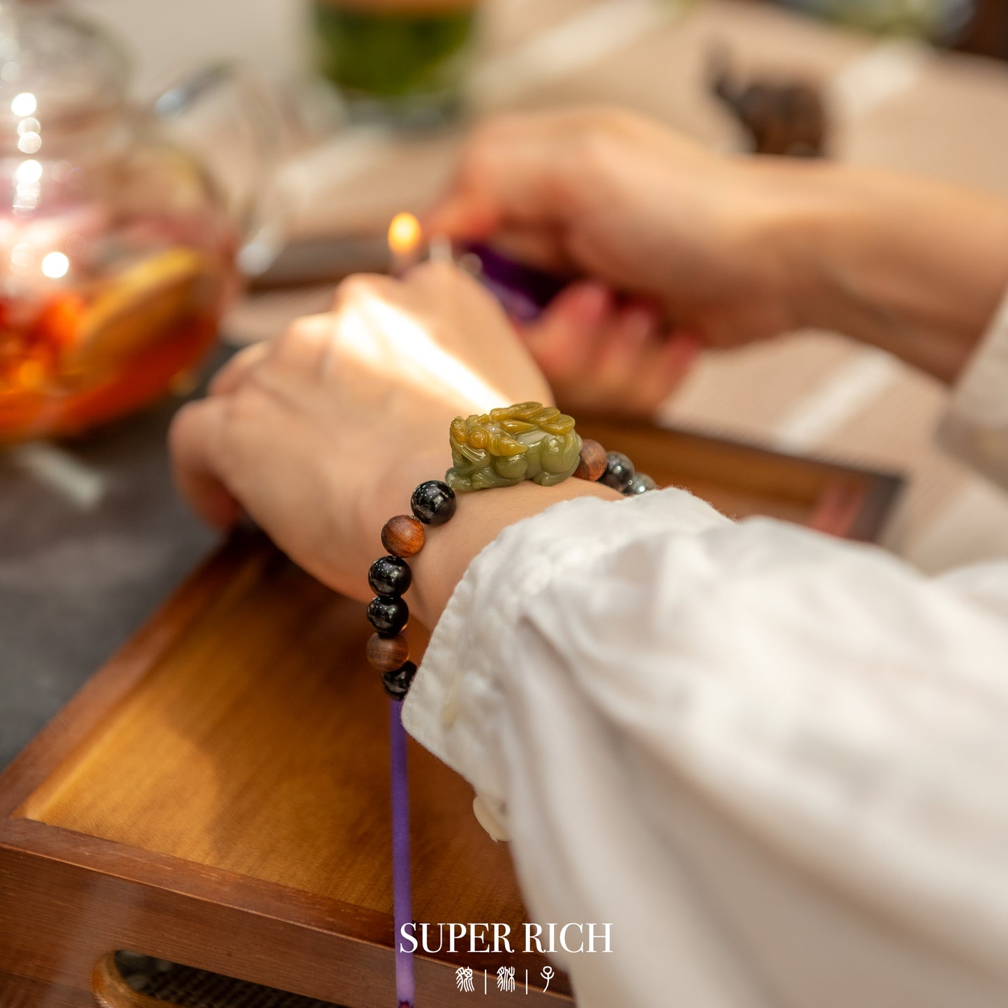 Person wearing a bracelet with colorful beads on a wooden table, with 'SUPER RICH' branding.