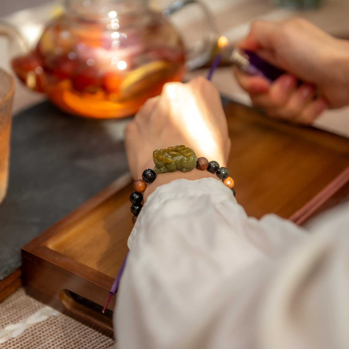 Person holding a beaded bracelet with a teapot and cup in the background