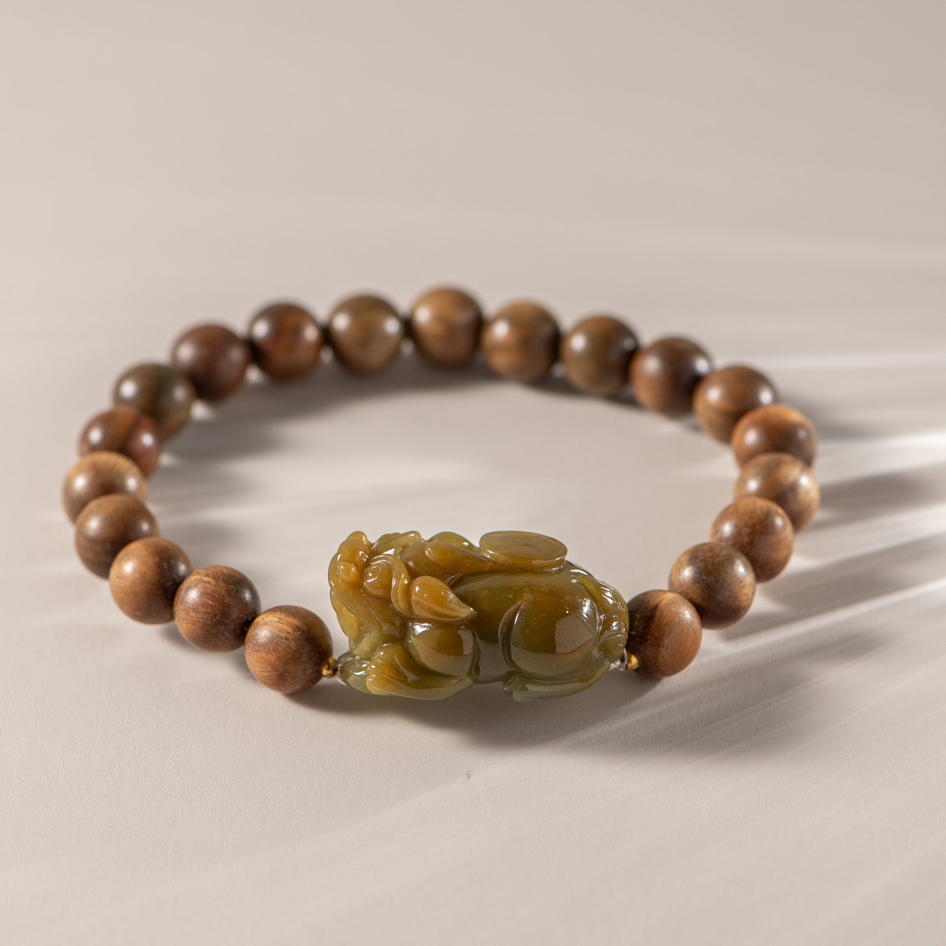 Wooden beaded bracelet with a green stone charm on a beige background