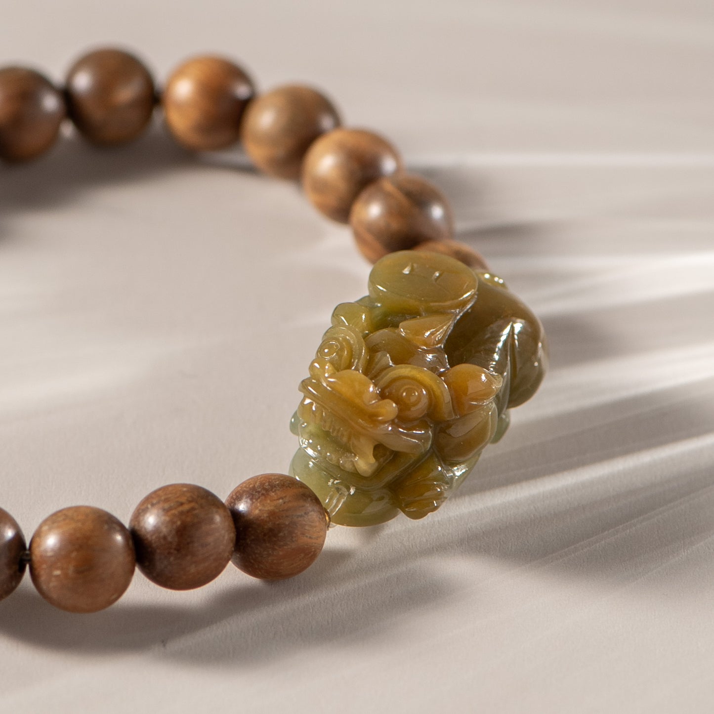 Wooden beaded bracelet with a large green stone on a beige fabric background